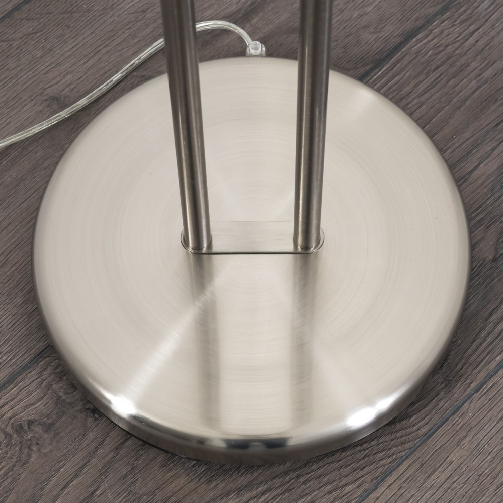 Runder, gebürsteter Metallfuß einer Stehlampe auf dunklem Holzboden.