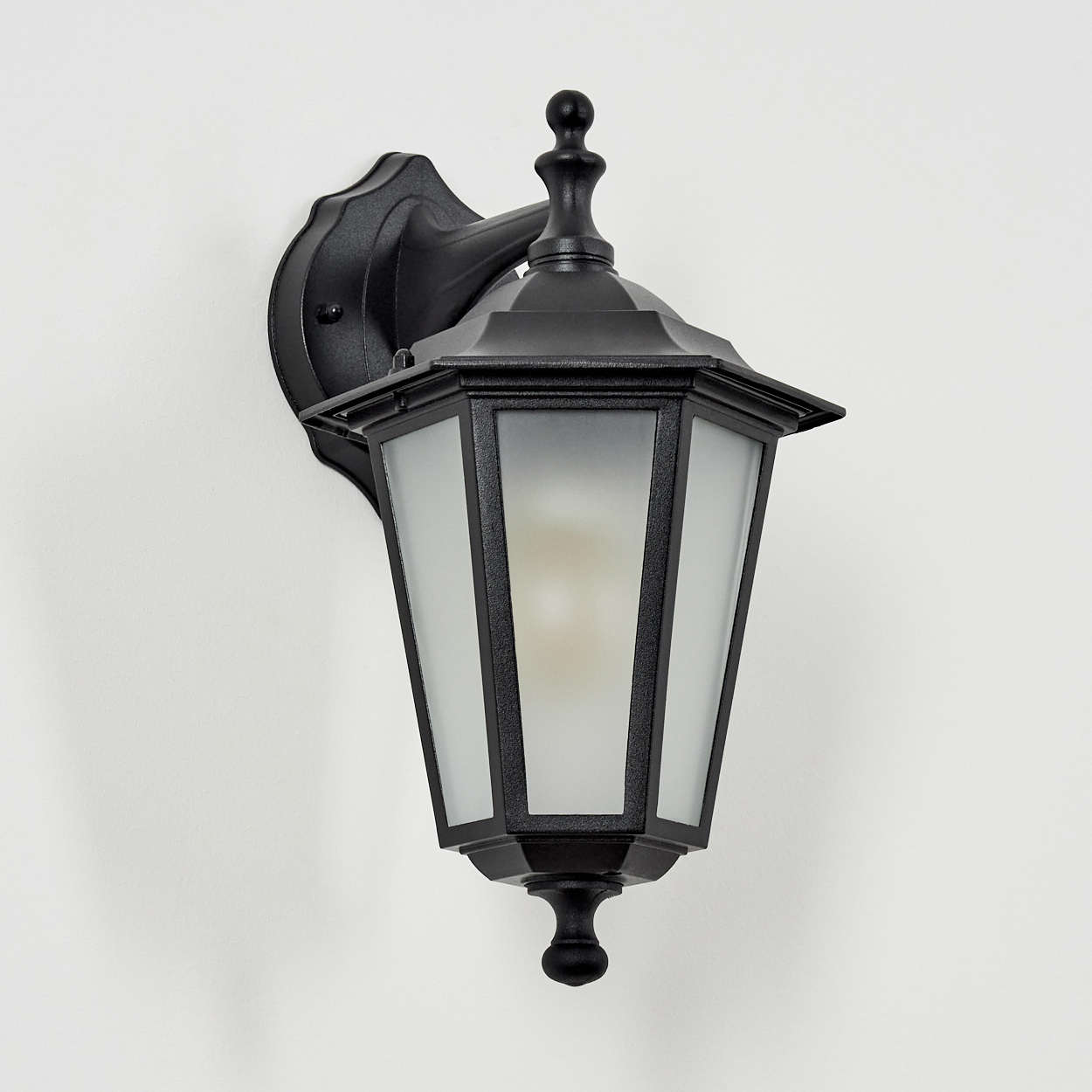 Eine schwarze Wandlampe mit mattem Glas und einem dekorativen Aufsatz.