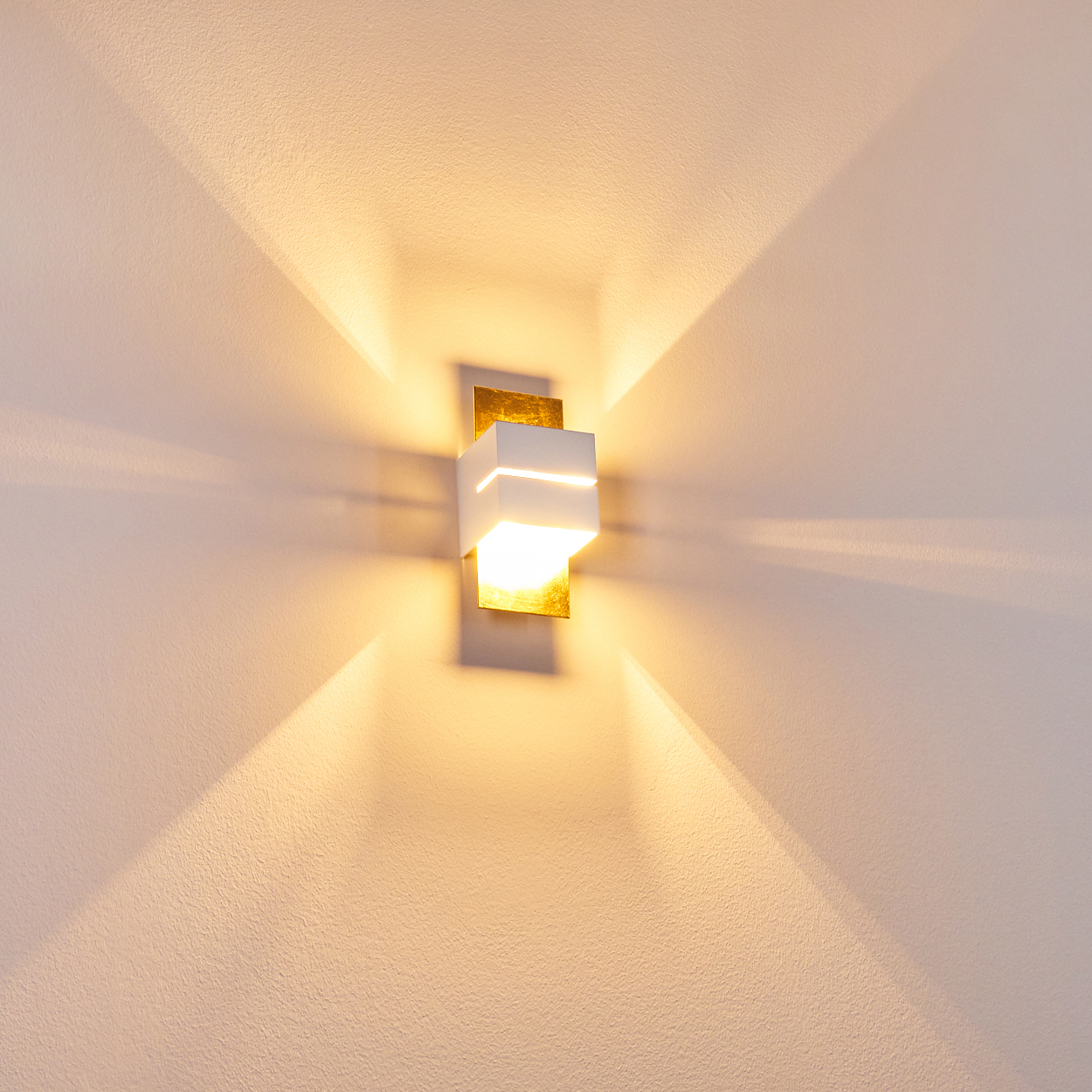 Eine weiße Wandleuchte mit Goldakzent leuchtet nach oben und unten an einer Wand.