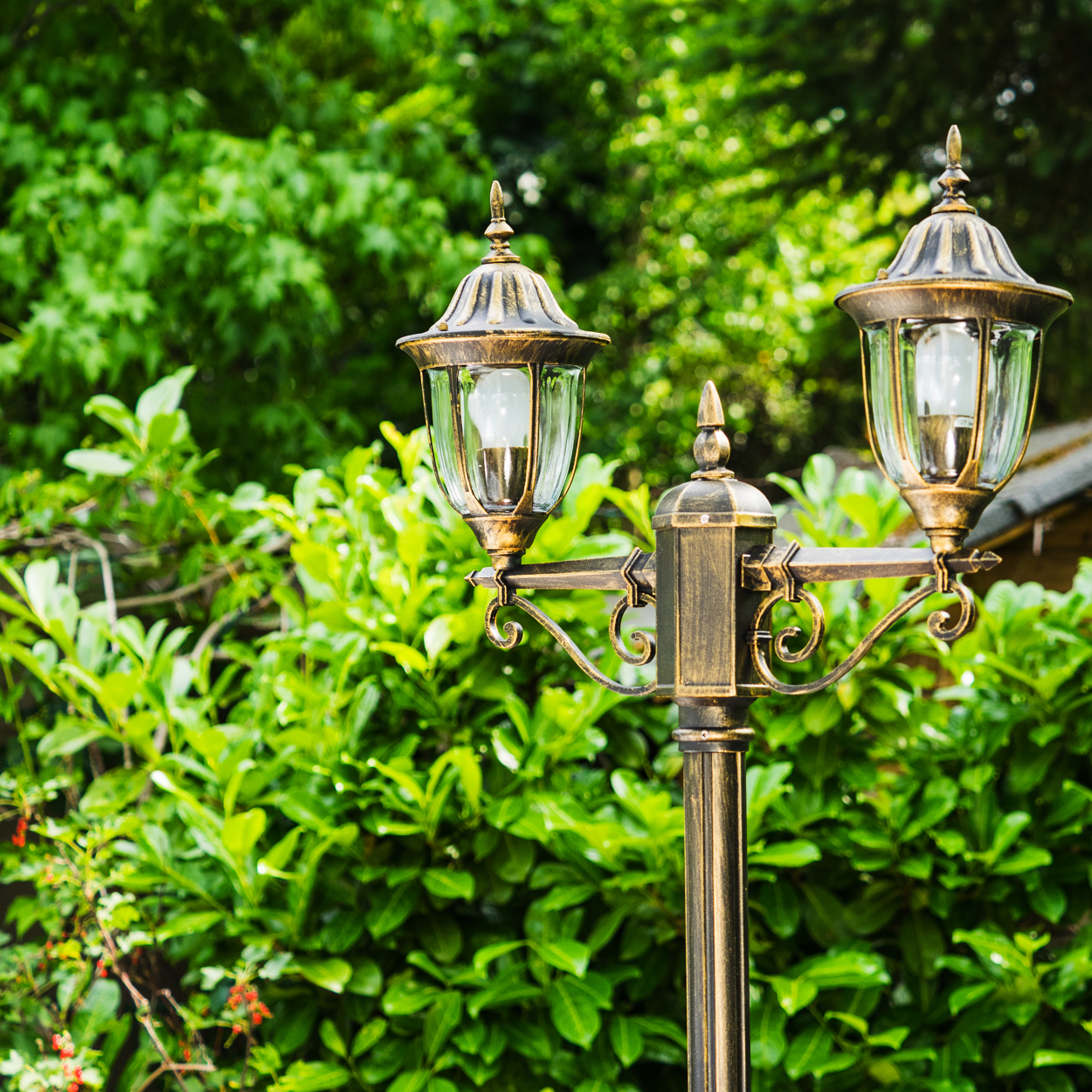 Zweigeschossige Lampe mit Glaslampenschirmen vor einem Hintergrund aus grünen Blättern.