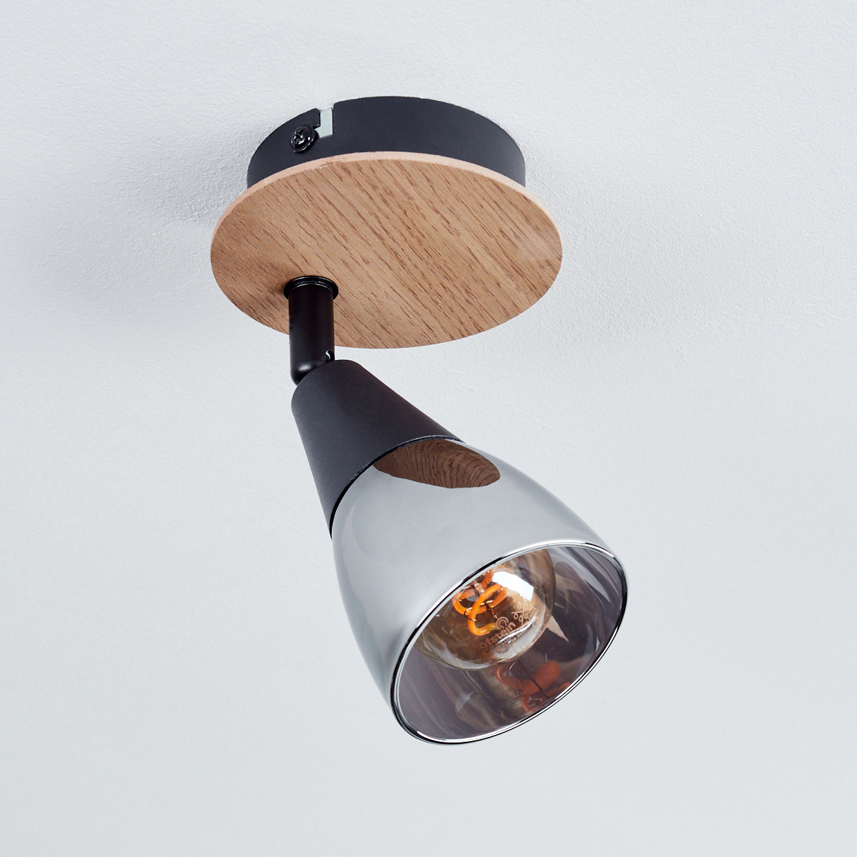 Eine Deckenleuchte mit Holzsockel, schwarzem Arm und glänzendem Metallsockel.