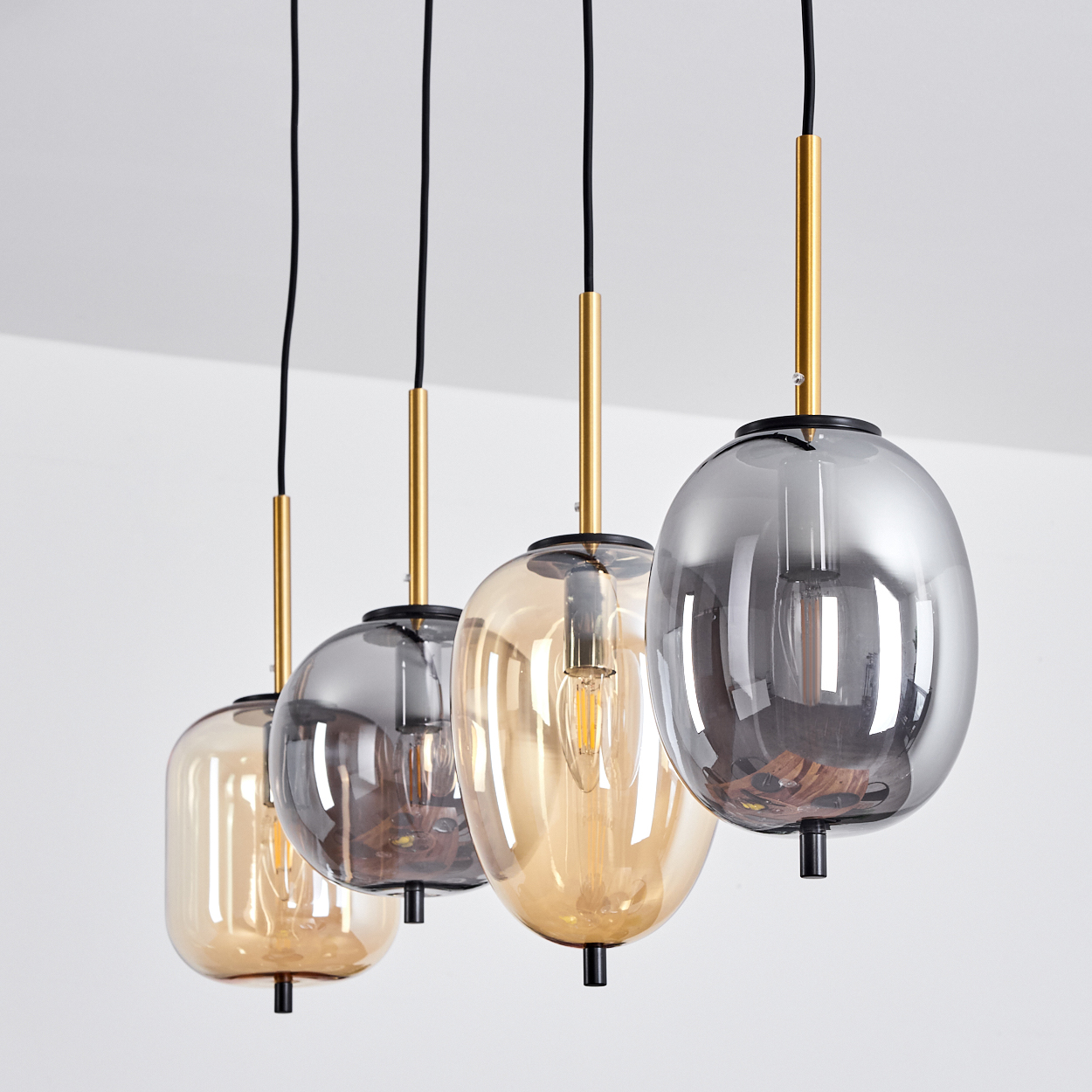 Vier moderne Pendelleuchten mit bernsteinfarbenen und grauen Glasschirmen, hängend an schwarzen Kabeln.