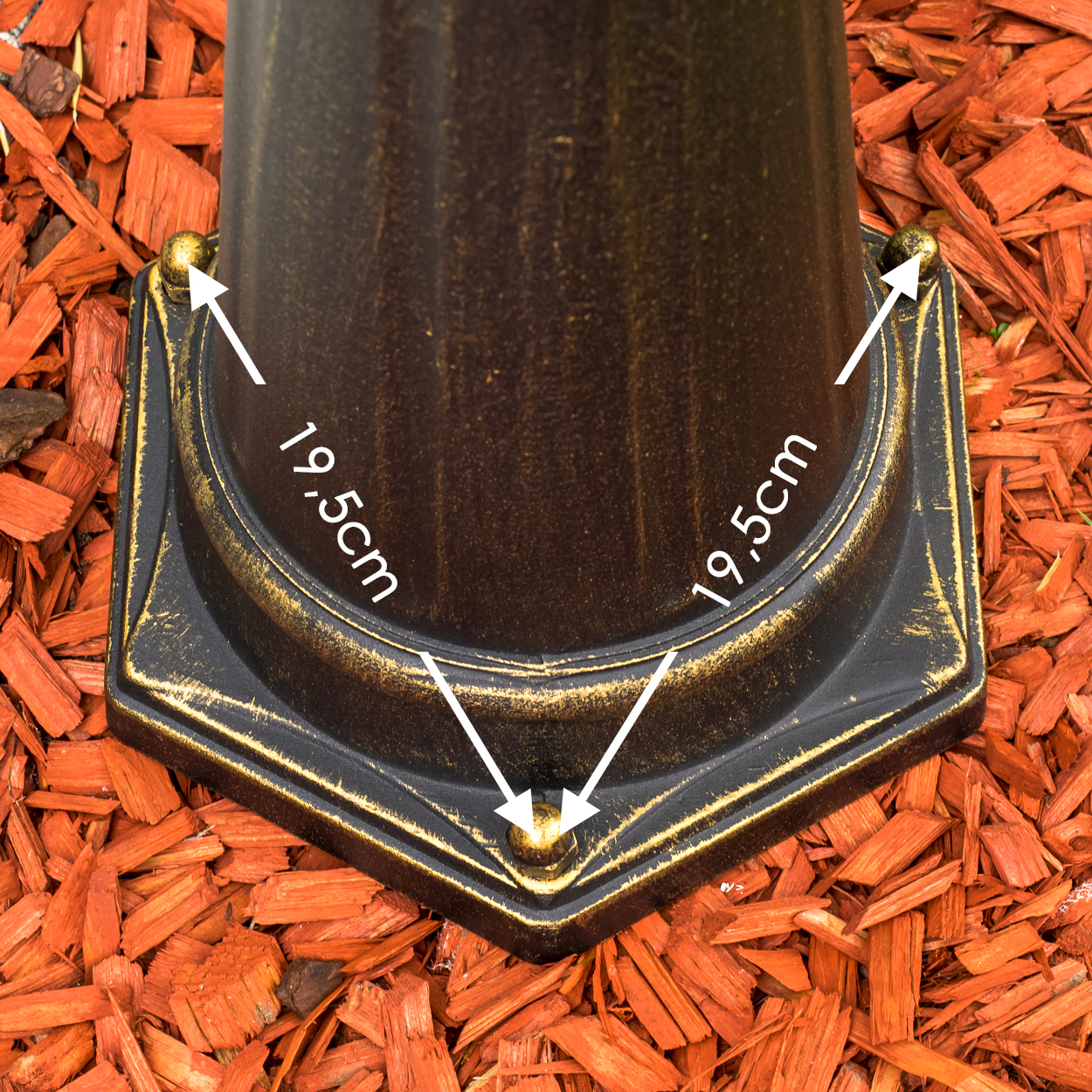 Ein bronzefarbener Sockel mit goldenen Akzenten, umgeben von rotem Rindenmulch.