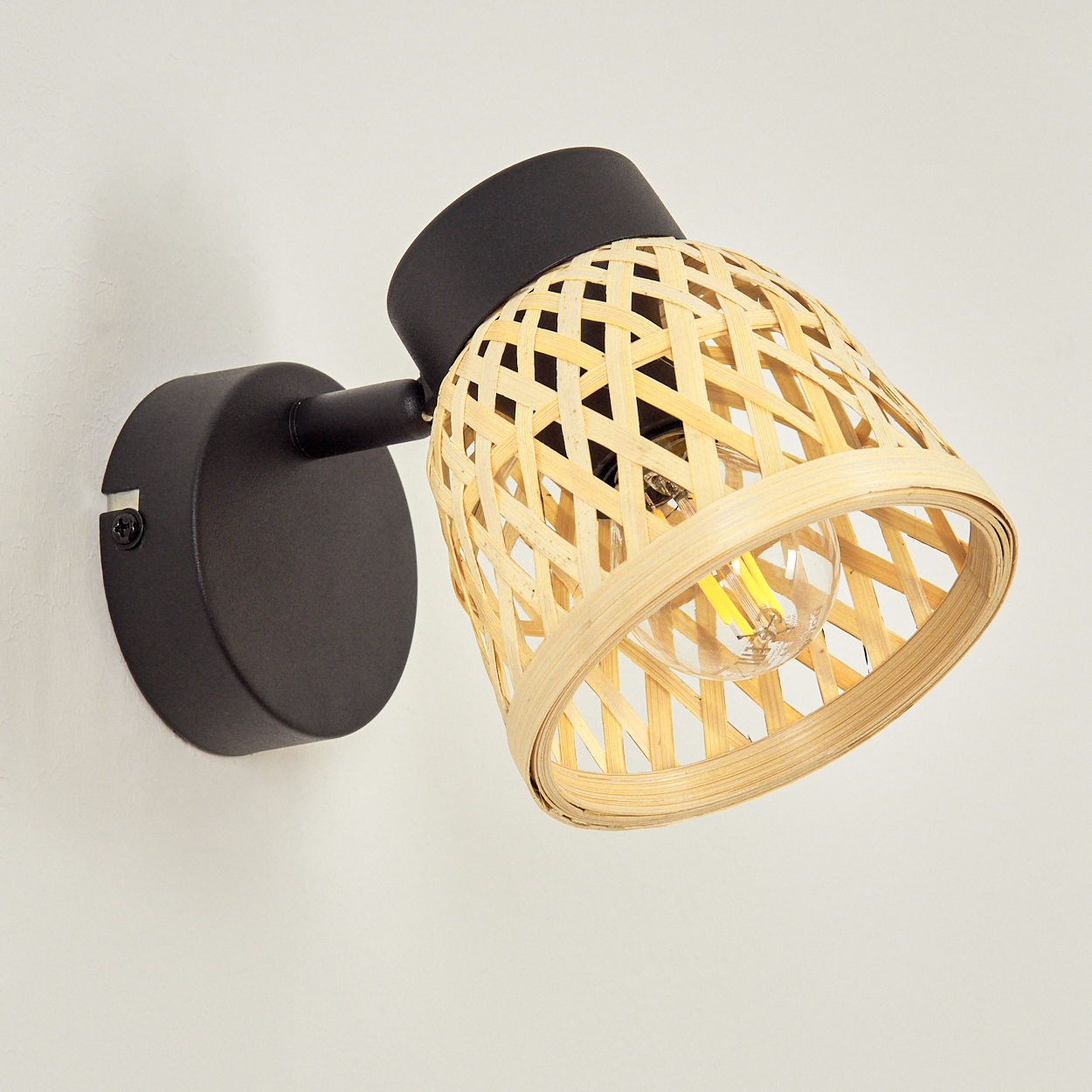 Eine schwarze Wandlampe mit einem geflochtenen Lampenschirm aus Bambus.