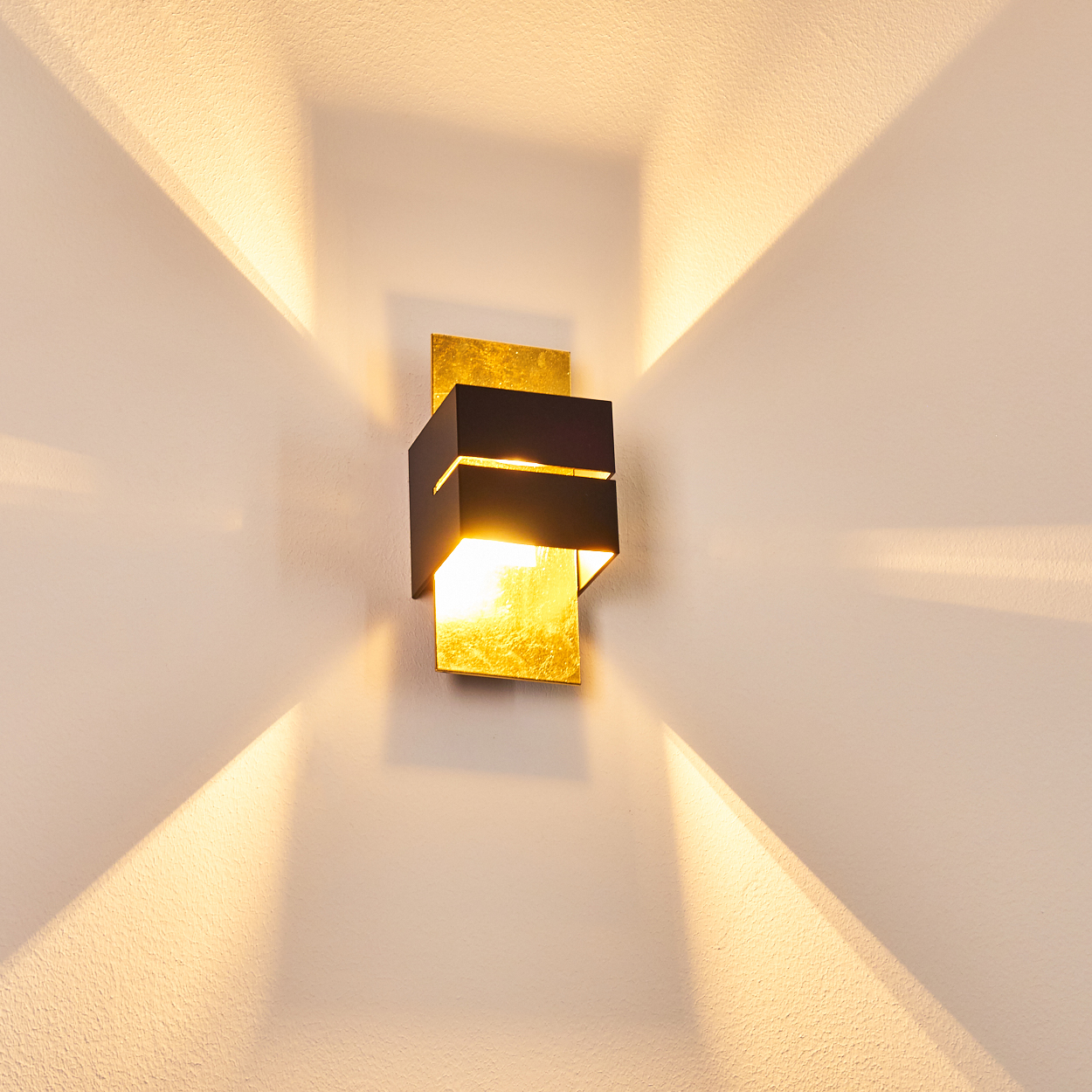 Eine schwarze Wandleuchte mit goldener Folie beleuchtet die Wand mit hellem Licht.