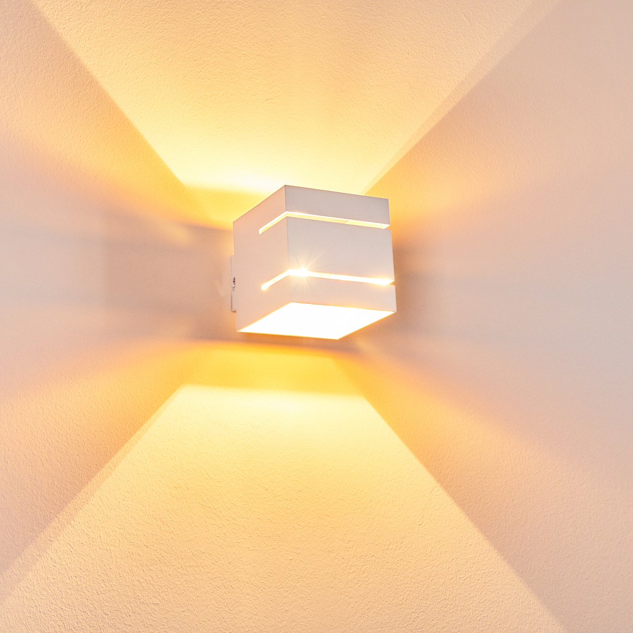 Ein weißer Würfel-Wandleuchter wirft warmes Licht nach oben und unten.