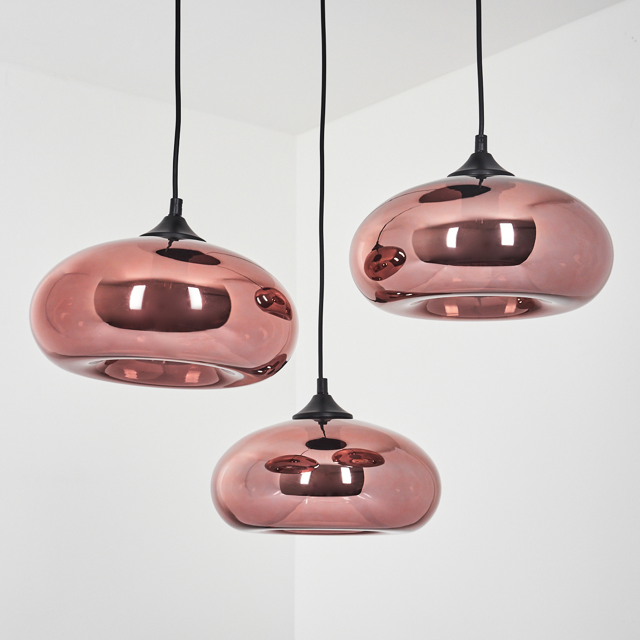 Drei roségoldene Pendelleuchten mit glatten, bauchigen Schirmen hängen von schwarzen Kabeln.