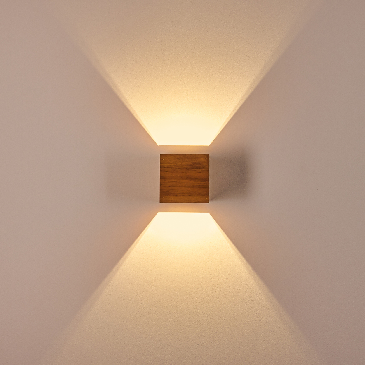 Ein würfelförmiger Wandleuchter aus Holz leuchtet nach oben und unten an einer hellen Wand.