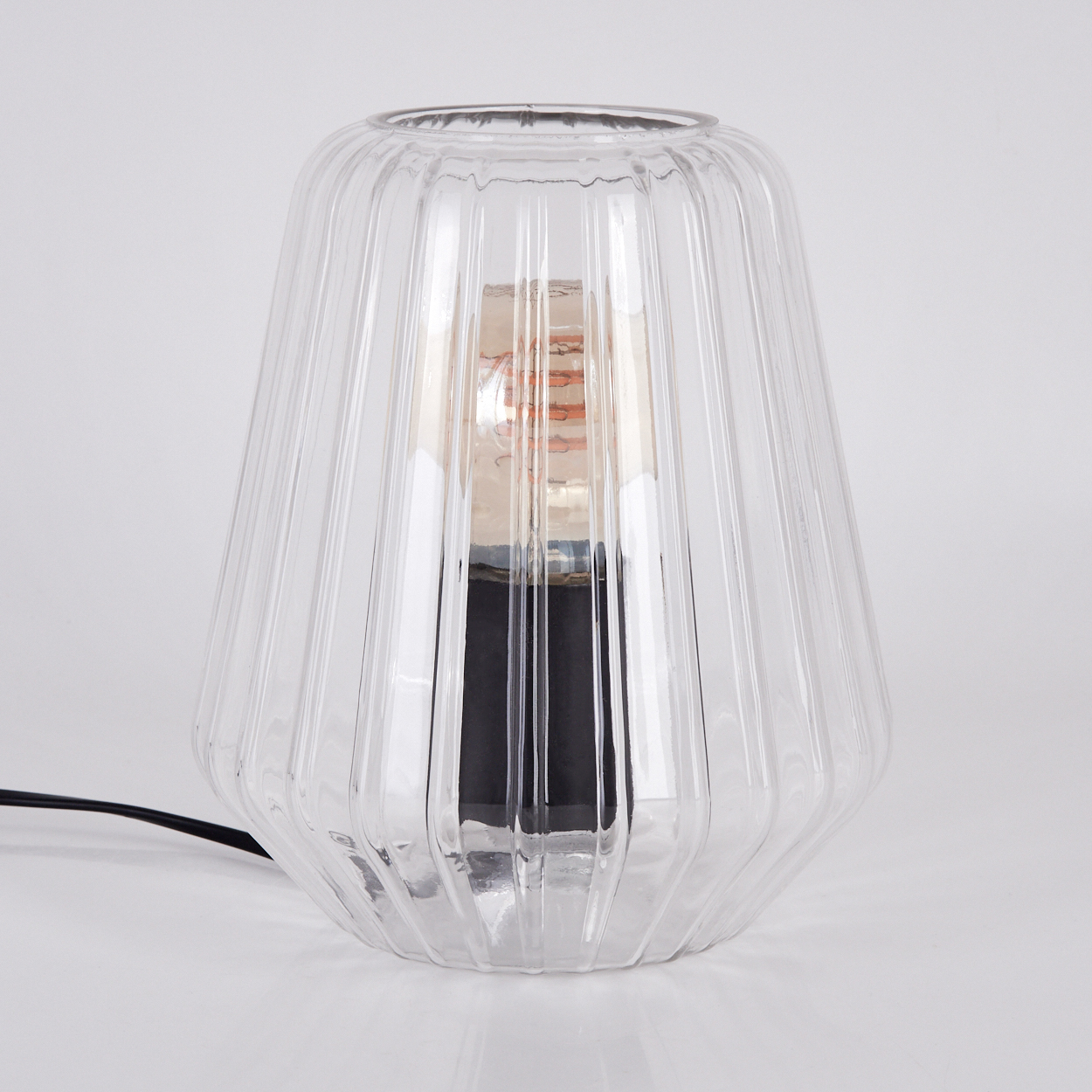 Eine durchsichtige geriffelte Glaslampe mit schwarzem Sockel und sichtbarem Glühfaden.