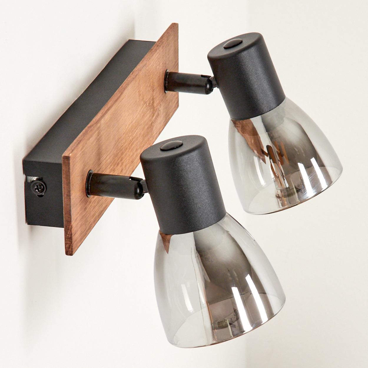 Eine moderne Wandleuchte mit Holzsockel und zwei verstellbaren schwarzen Strahlern mit Rauchglas.