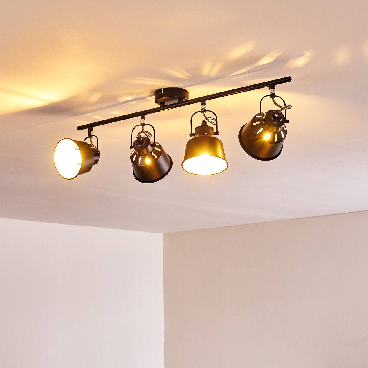Eine schwarze Deckenleuchte mit vier verstellbaren Spots, die Licht auf die Decke werfen.