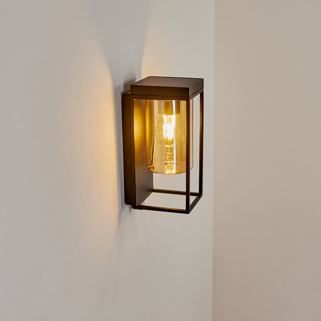 Eine dunkle Wandleuchte mit einem bernsteinfarbenen Glaszylinder und Glühbirne.