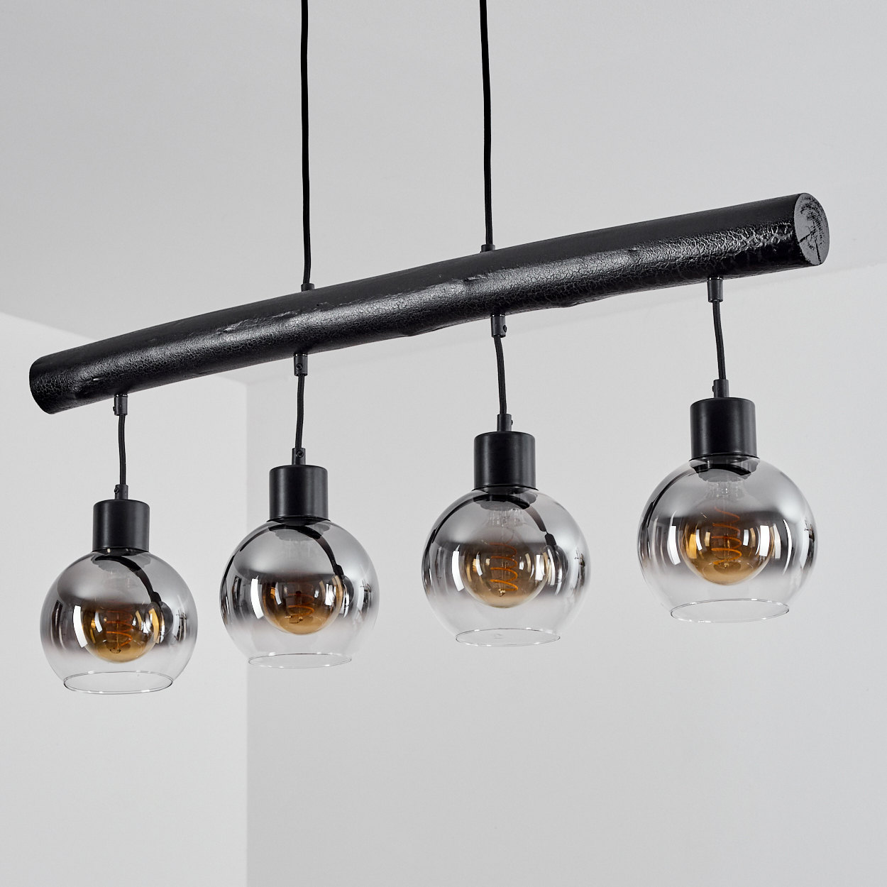 Eine schwarze Pendelleuchte mit vier runden Glaslampenschirmen und Glühbirnen.
