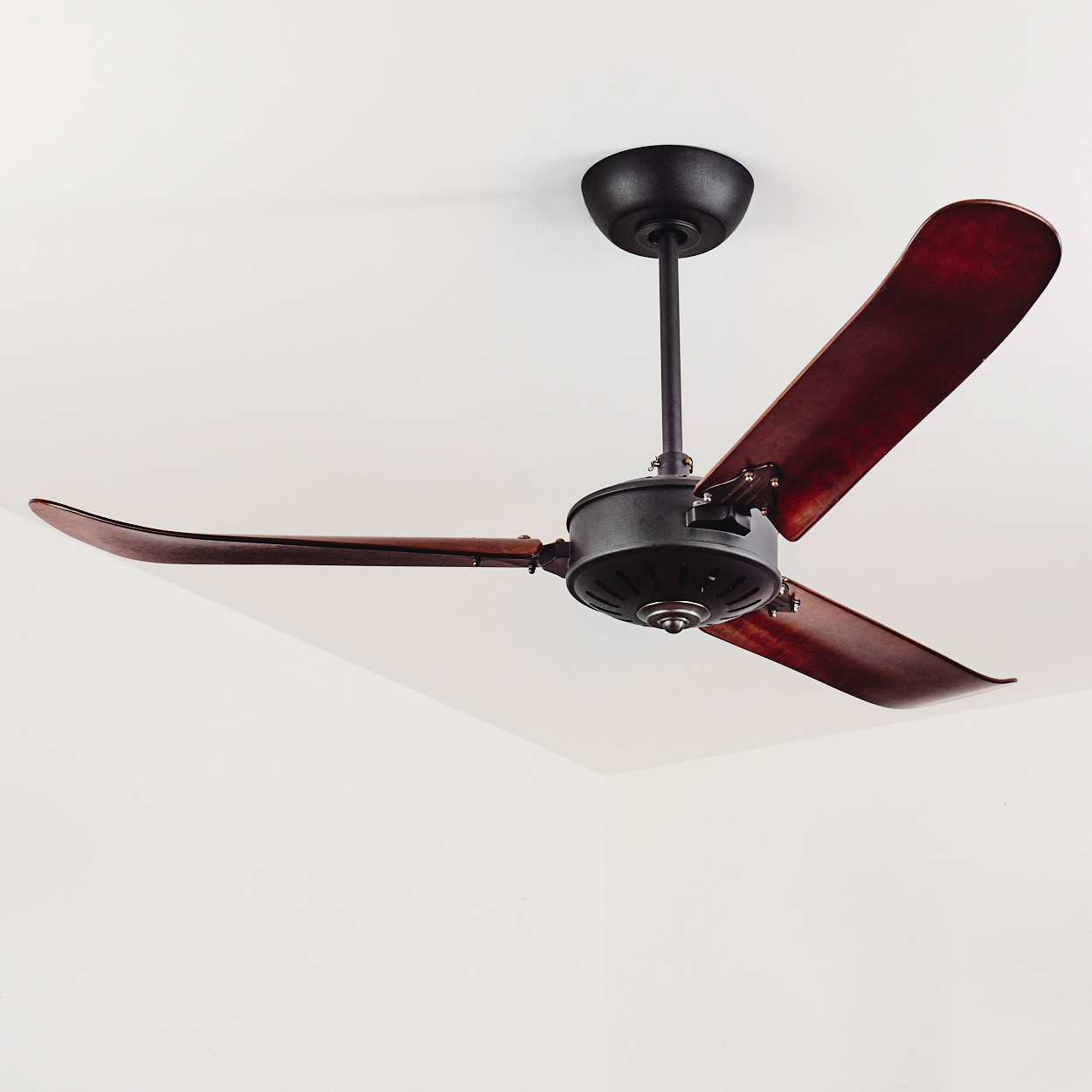 Ein dunkler Deckenventilator mit drei Holzblättern hängt an einer weißen Decke.