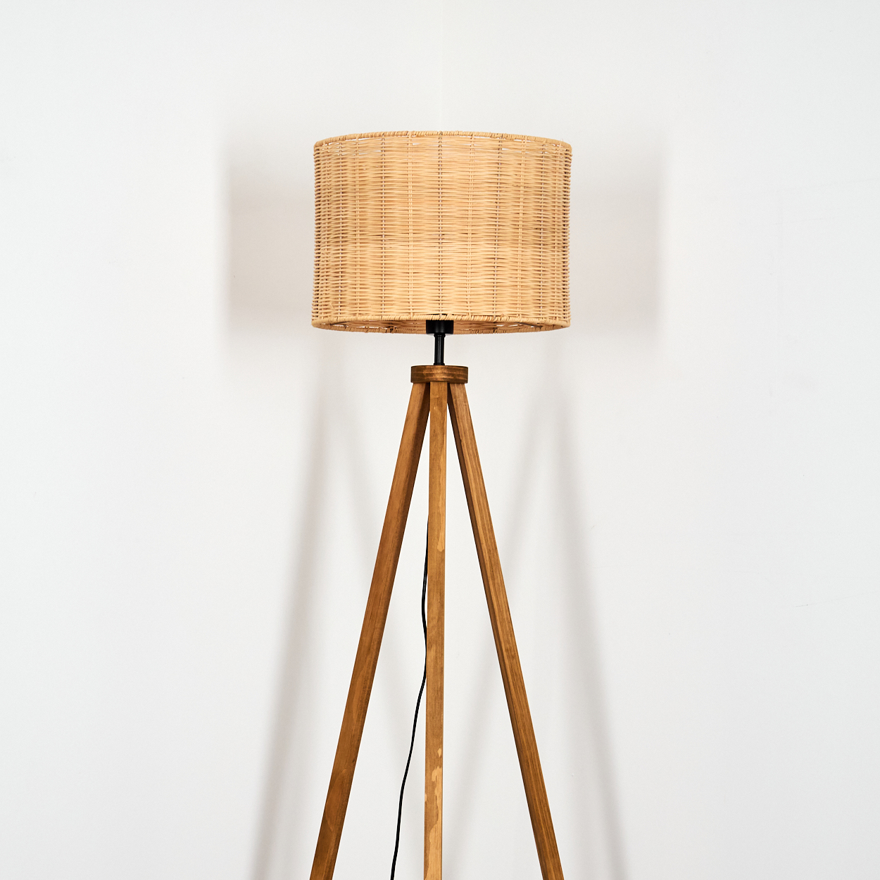 Ein Stehlampenfuß aus Holz mit drei Beinen und einem Lampenschirm aus Weidengeflecht.