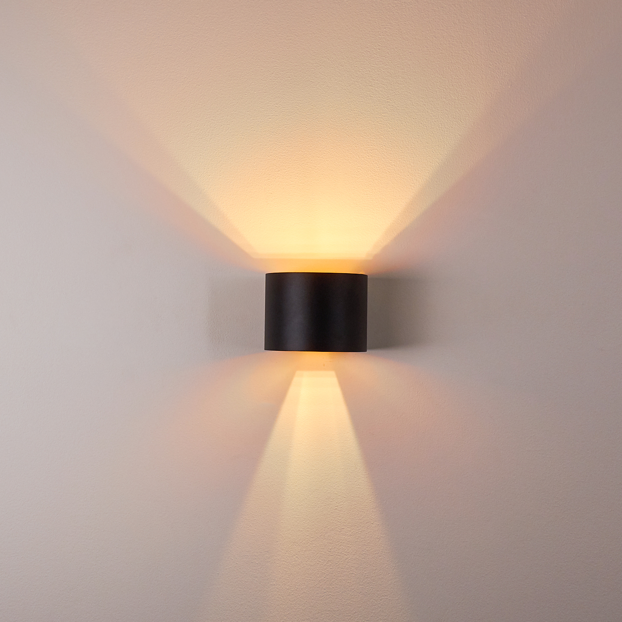 Schwarze Wandleuchte wirft nach oben und unten Lichtkegel auf eine weiße Wand.