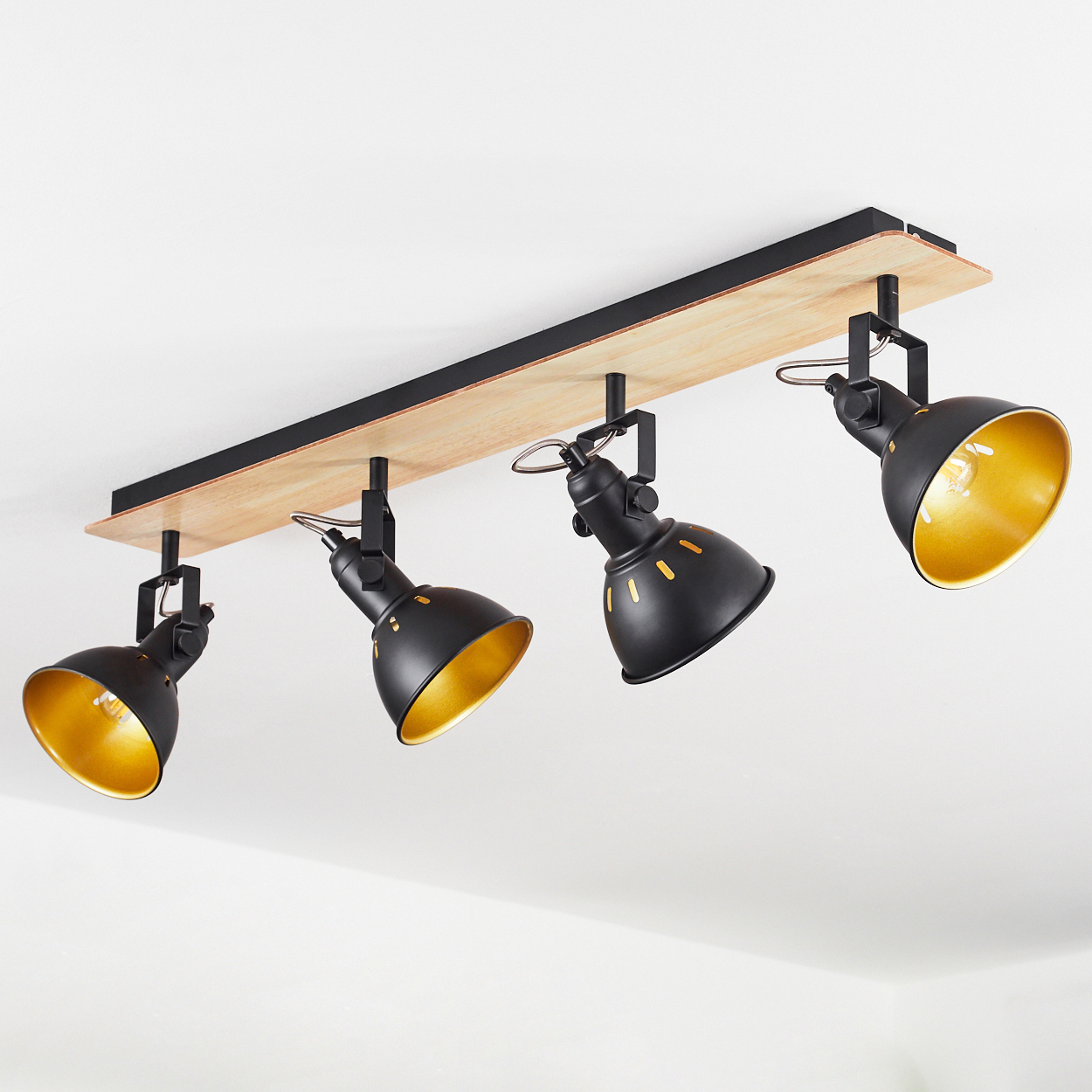 Eine Deckenleuchte mit vier schwarzen Spots mit goldener Innenseite auf einem Holzbrett.