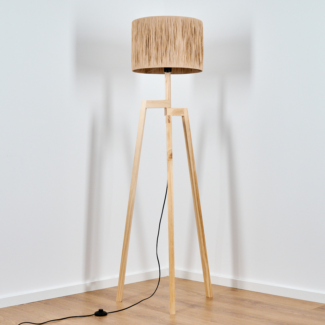 Ein Stehleuchte mit Holzstativ und geflochtenem Lampenschirm steht in einer Ecke.