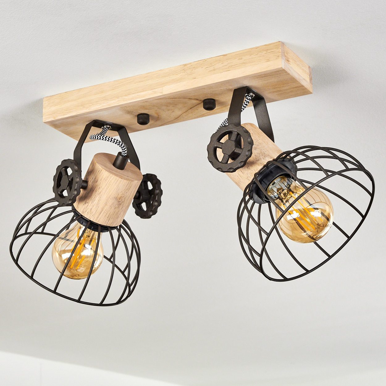 Deckenleuchte mit Holzsockel, zwei verstellbaren Armen mit schwarzen Drahtkörben und Glühbirnen.