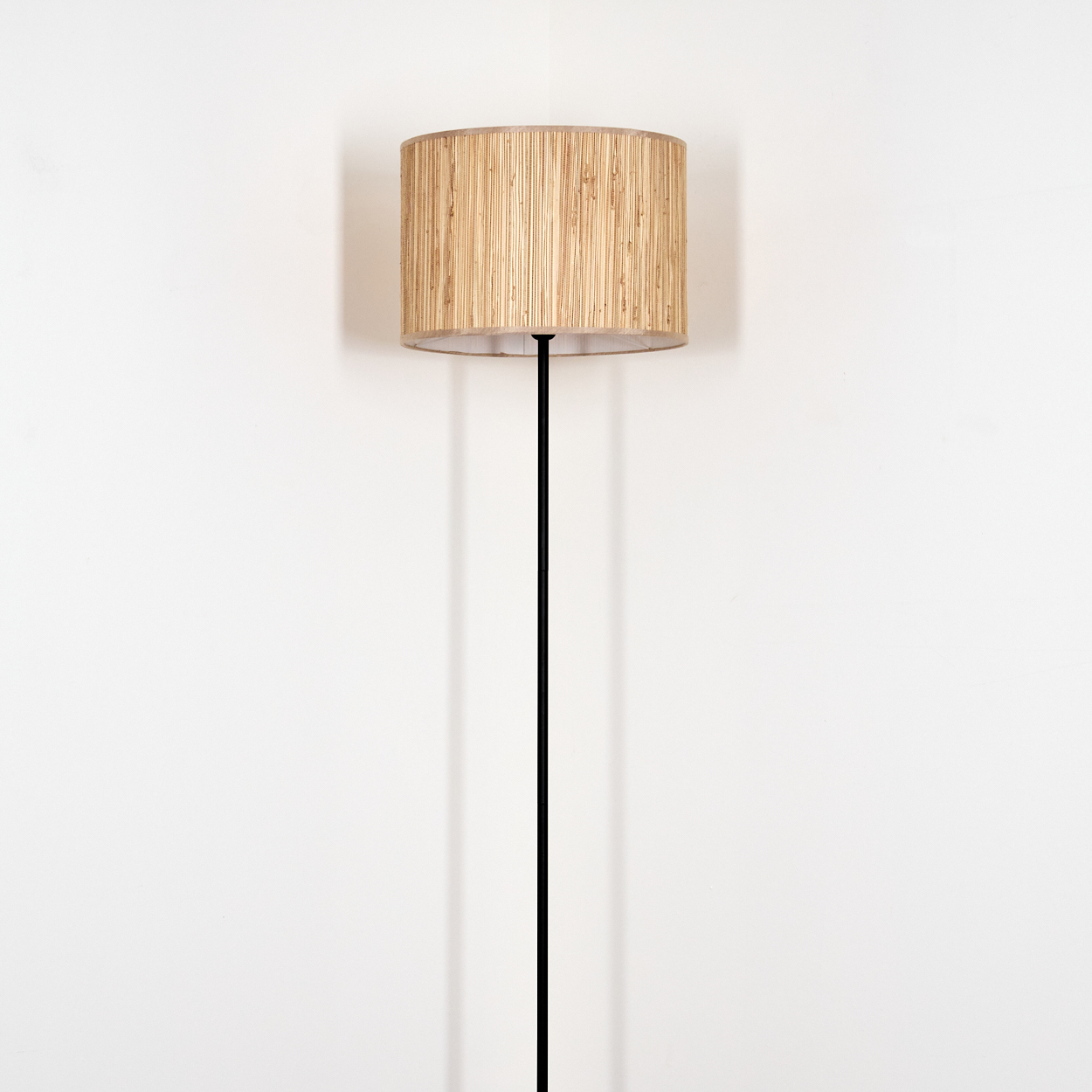 Eine Stehlampe mit einem Lampenschirm aus natürlichen Fasern und einem schwarzen Stab.
