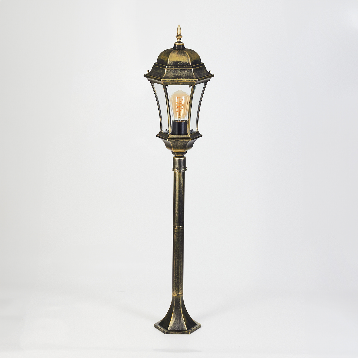 Eine goldene und schwarze Stehlampe mit Glas und Glühbirne auf weißem Grund.
