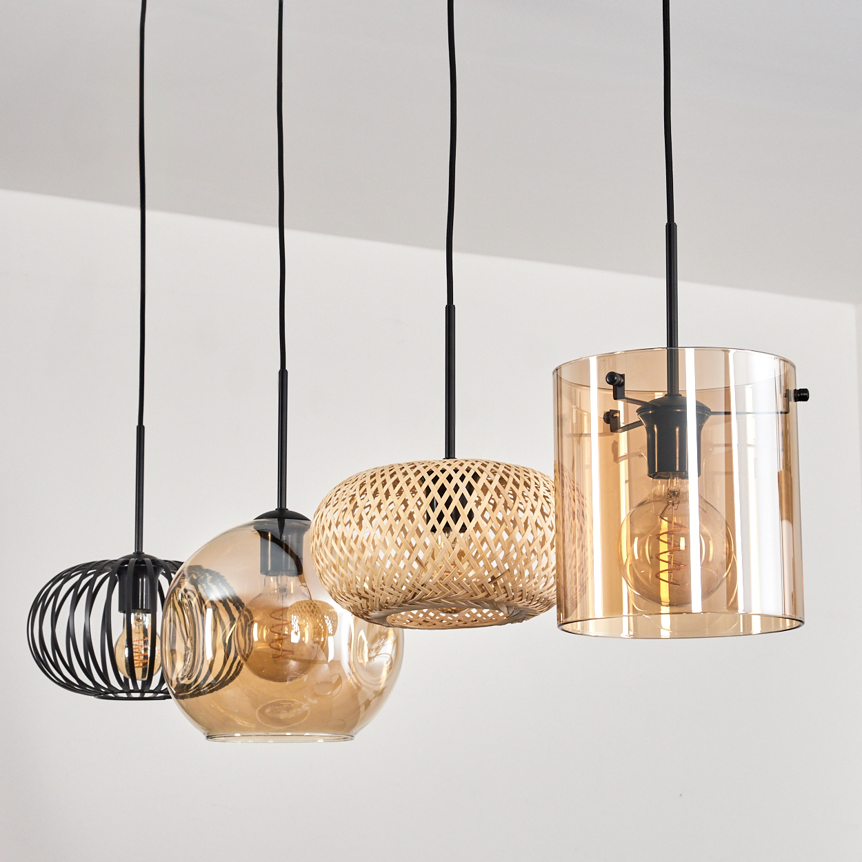 Vier Pendelleuchten mit Glas-, Bambus- und Metallschirmen hängen vor einer weißen Wand.