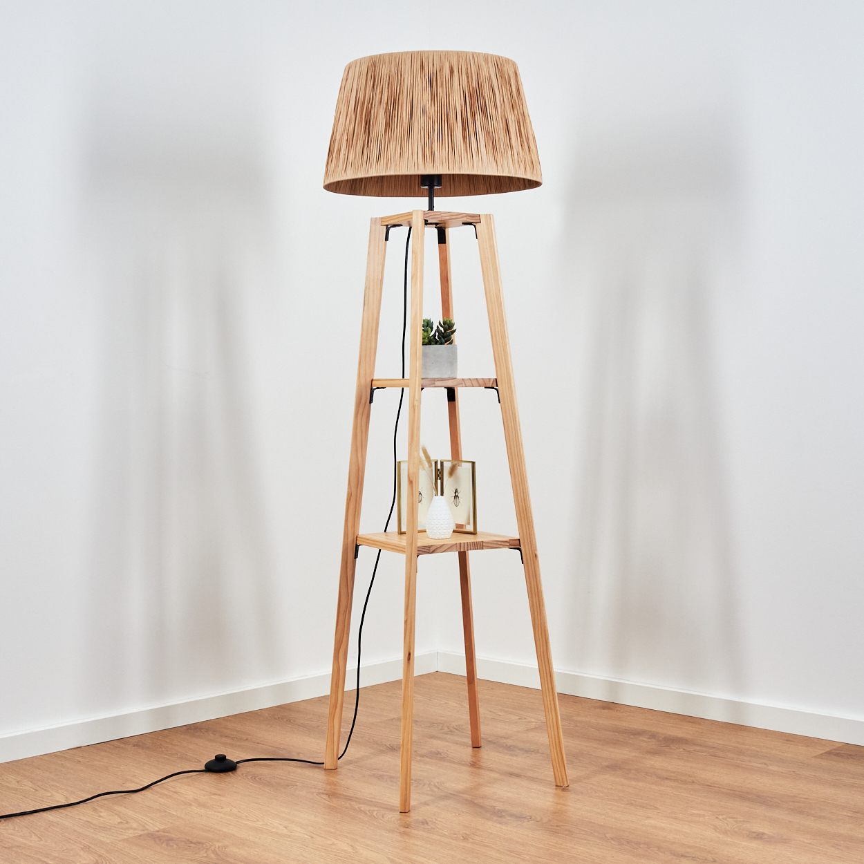 Eine Holzstehlampe mit gewebtem Schirm steht in einer Ecke, mit Regalen und Deko.