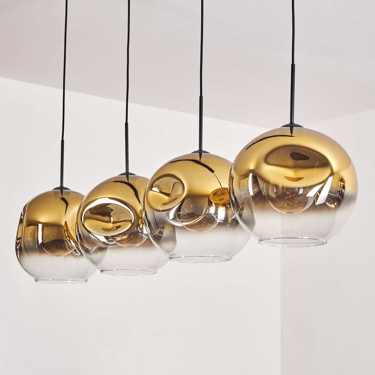 Vier goldene Pendelleuchten mit transparenten Glaskugeln hängen an schwarzen Kabeln.