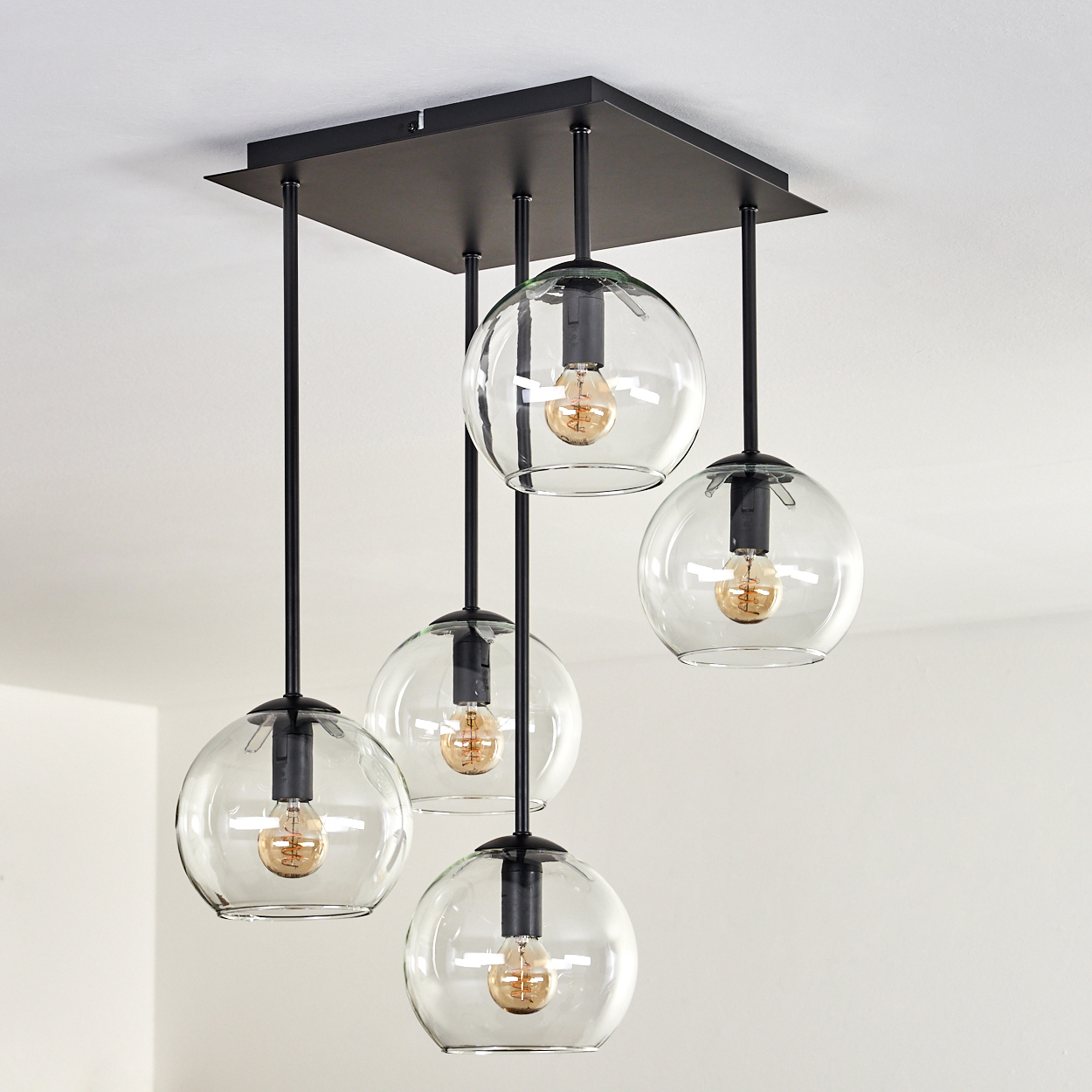 Eine moderne schwarze Hängeleuchte mit fünf klaren Glaskugeln und Edison-Glühbirnen.