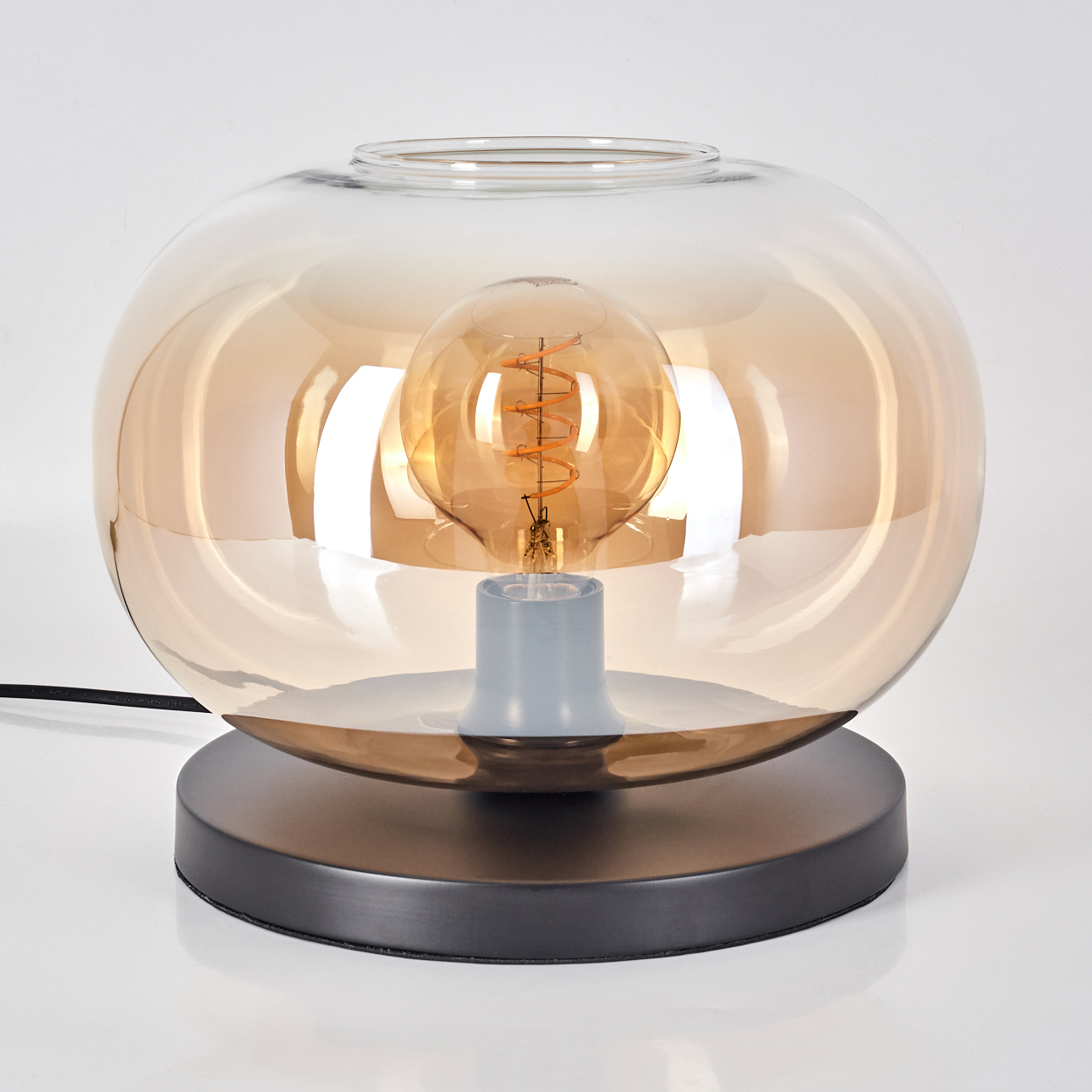 Eine bernsteinfarbene Glas-Tischlampe mit einem sichtbaren Glühfadenbirne.