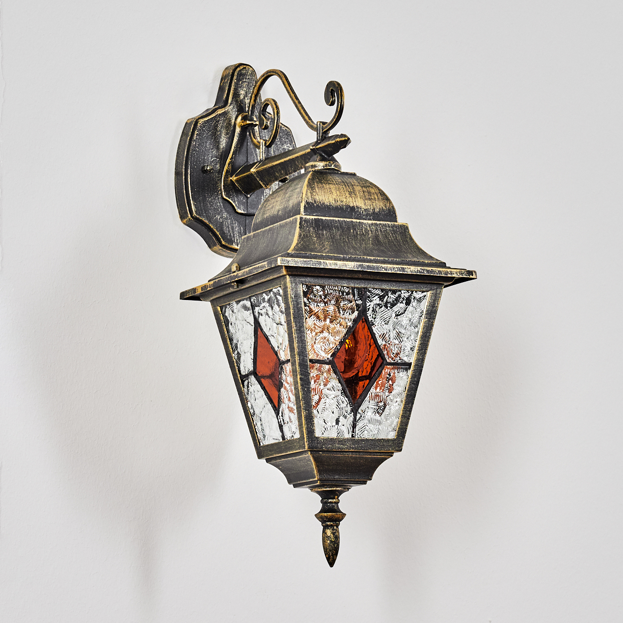 Eine Wandlaterne aus dunklem Metall mit Glasfenstern und roten Rauten.