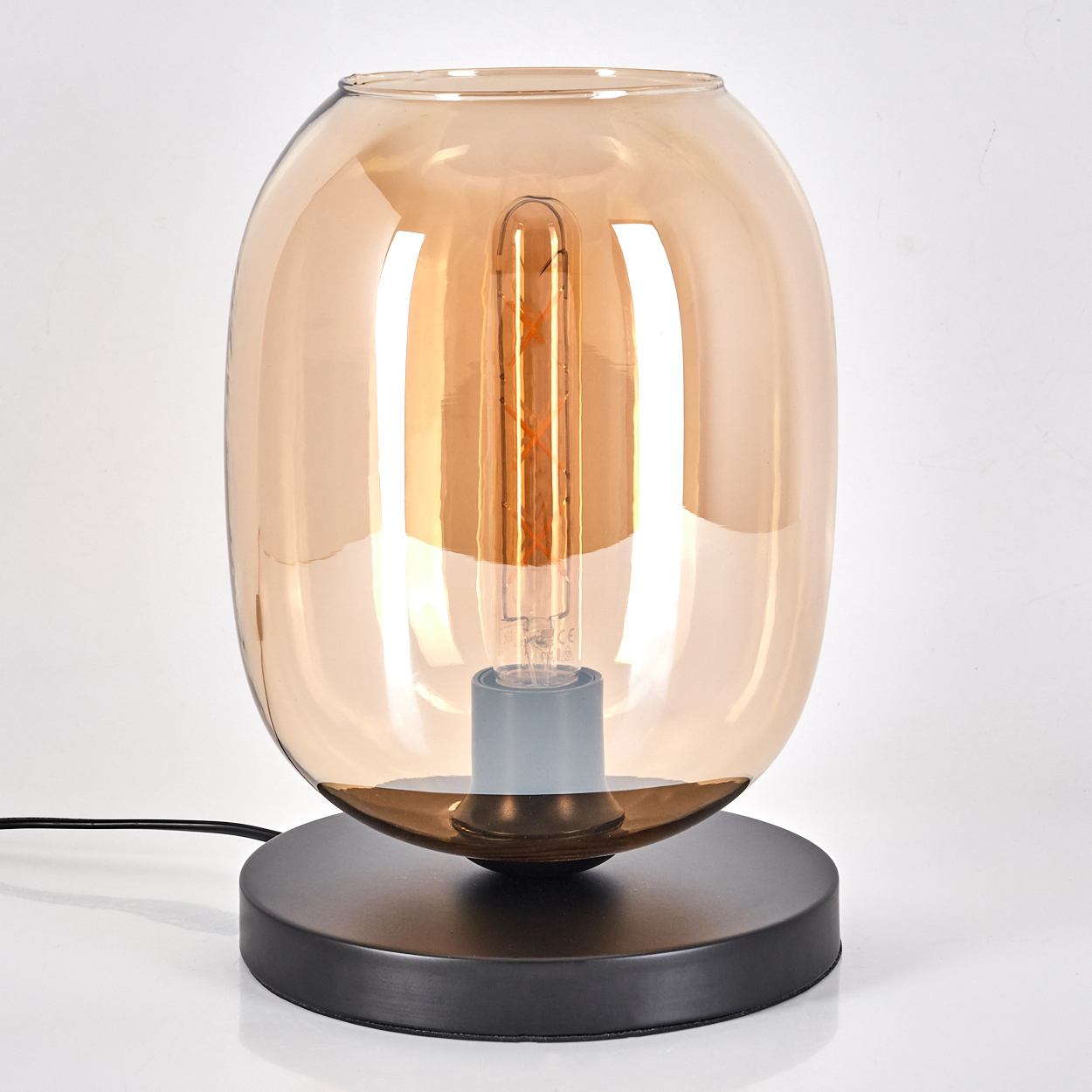 Eine moderne bernsteinfarbene Glas-Tischlampe mit schwarzem Sockel und Glühfadenbirne.