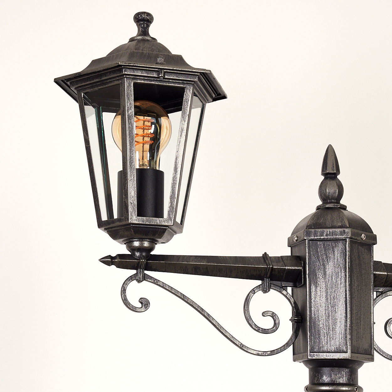 Vintage schwarze Straßenlaterne mit verzierten Spiralen und beleuchteter Edison-Birne.