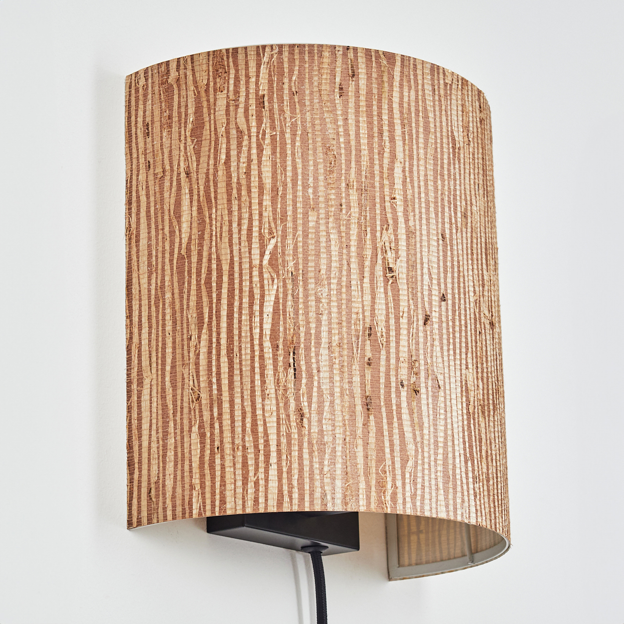 Eine zylindrische Wandleuchte mit einer Schirmummantelung aus Rattan mit vertikalen Streifen aus hellem und dunklem Braun.