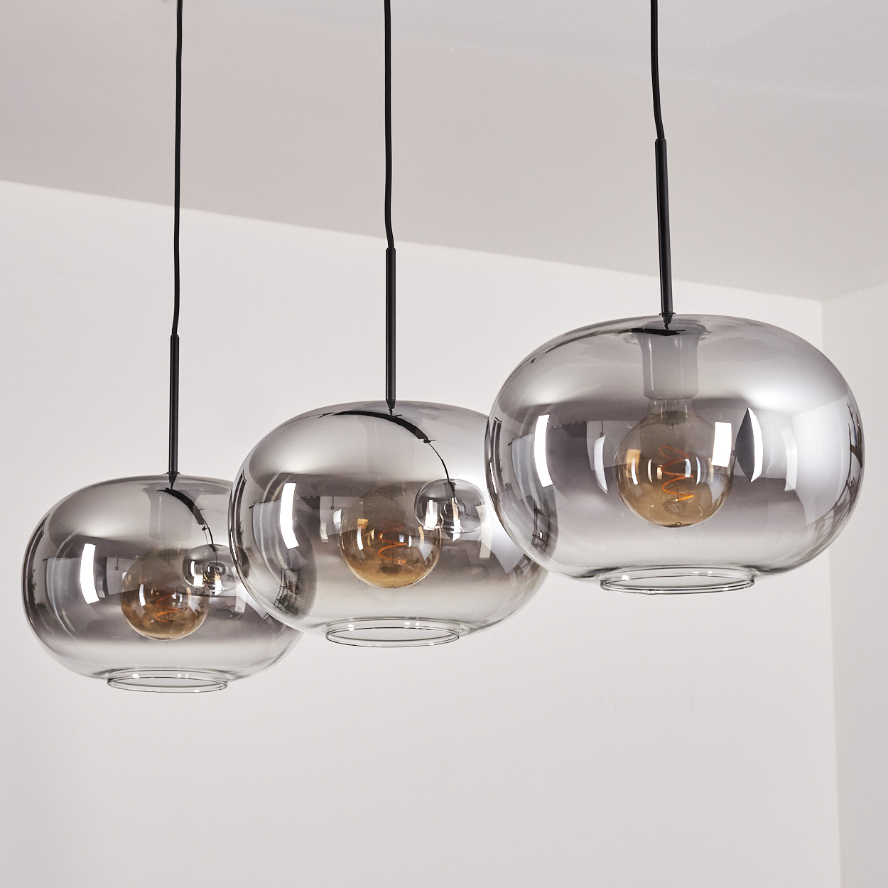Drei rauchglas Pendelleuchten mit Glühbirnen hängen von schwarzen Kabeln.
