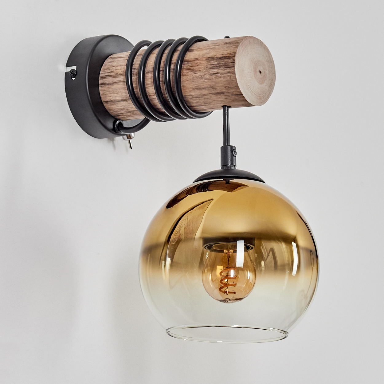 Wandleuchte mit Holzstamm, schwarzen Spiralen und bernsteinfarbener Glaskugel.