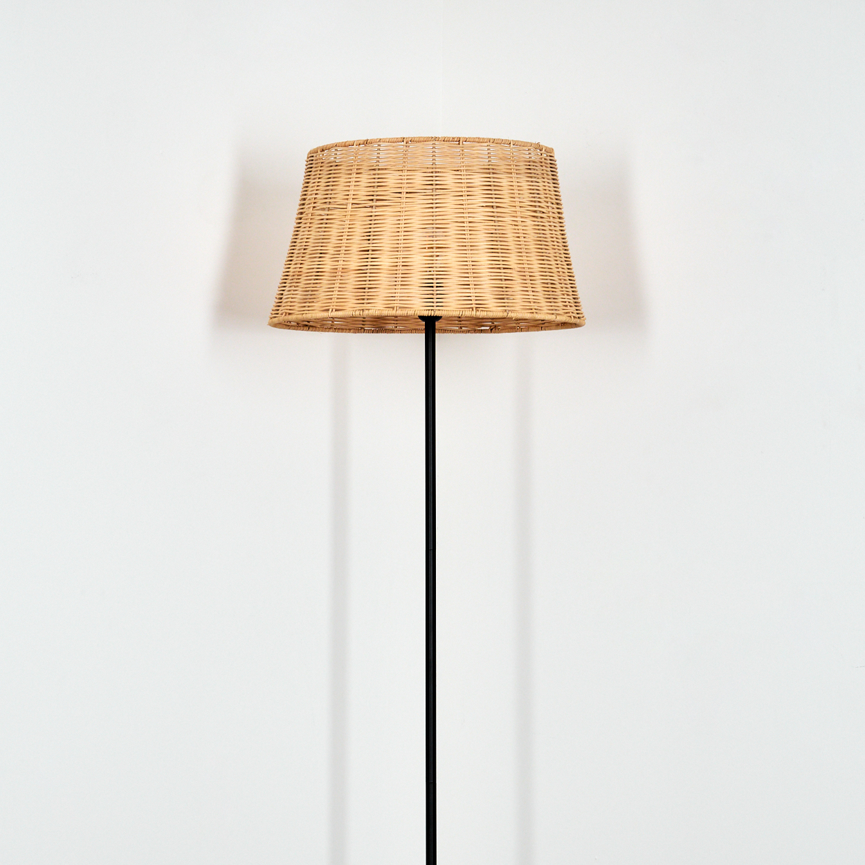 Ein runder, geflochtener Lampenschirm aus hellem Holz auf einem schwarzen Ständer.