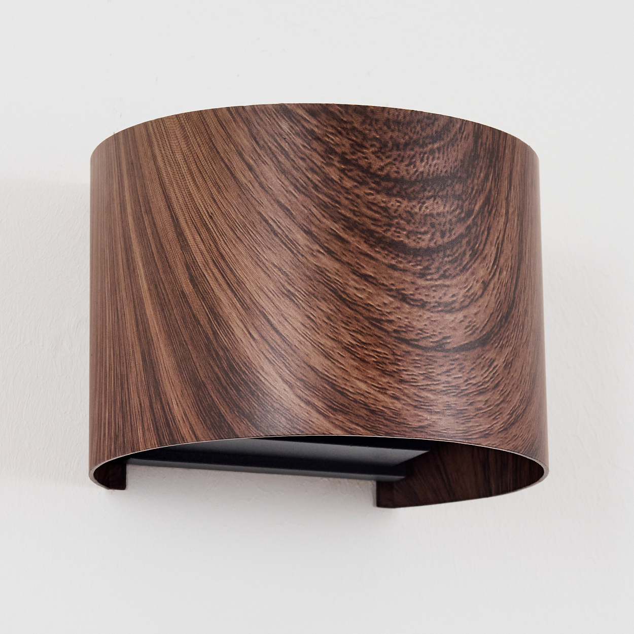 Eine braune Wandleuchte mit Holzmaserungsmuster hängt an einer weißen Wand.