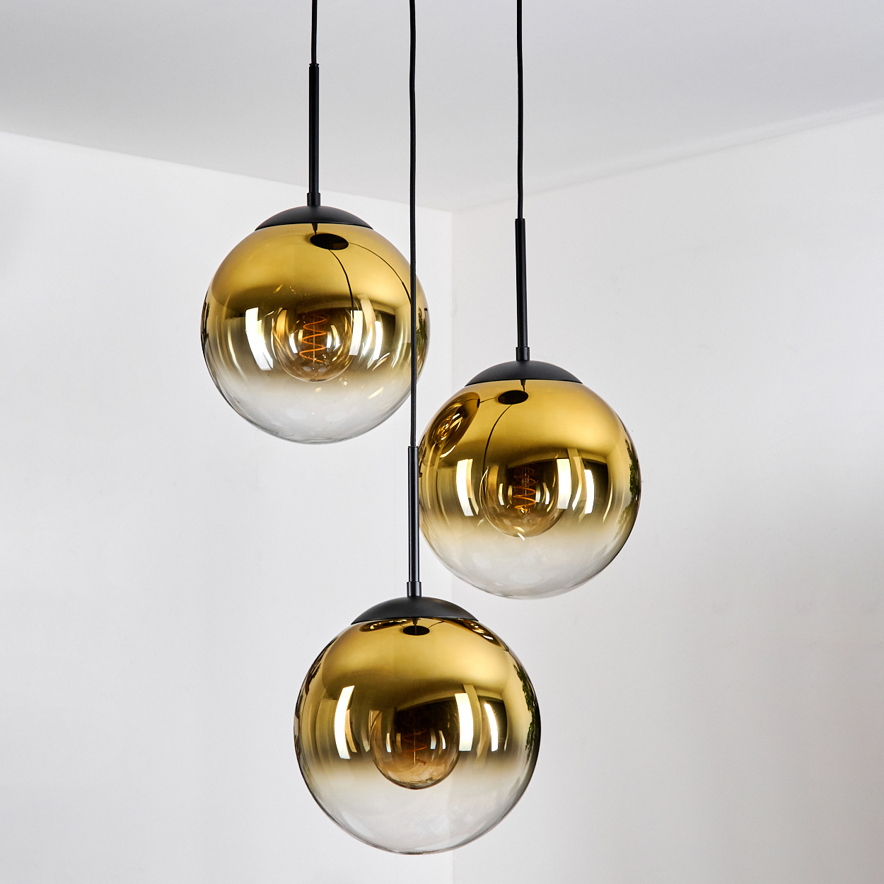 Drei goldene Hängeleuchten mit Glaskugeln und sichtbaren Glühbirnen.