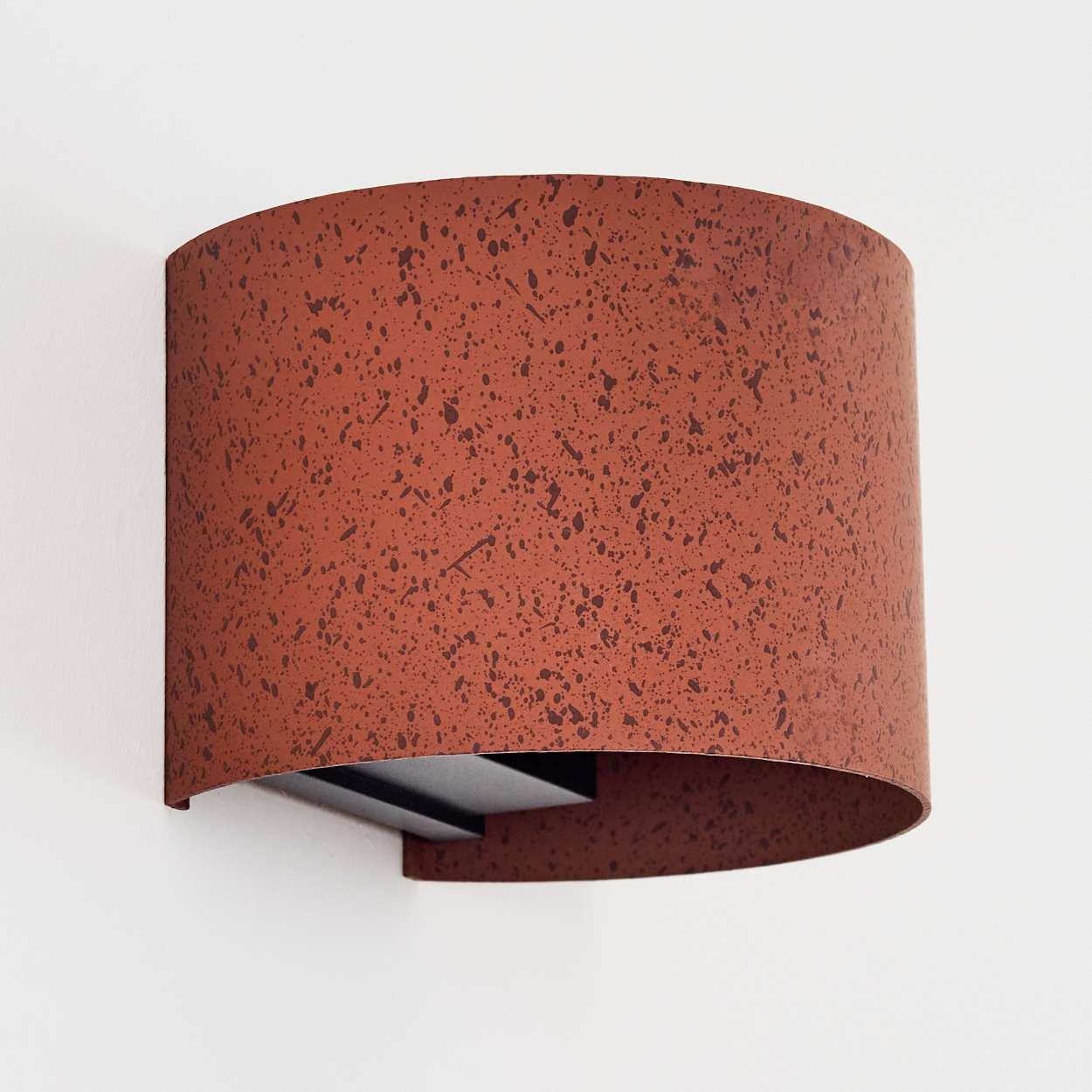 Ein korallenroter Wandleuchter mit dunklen Sprenkeln, an einer weißen Wand montiert.