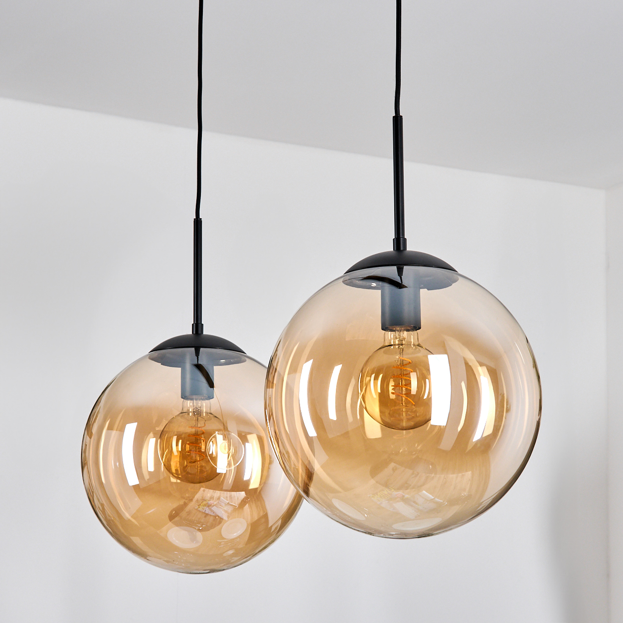 Zwei bernsteinfarbene Glaskugel-Pendelleuchten mit Edison-Glühbirnen hängen an schwarzen Kabeln.
