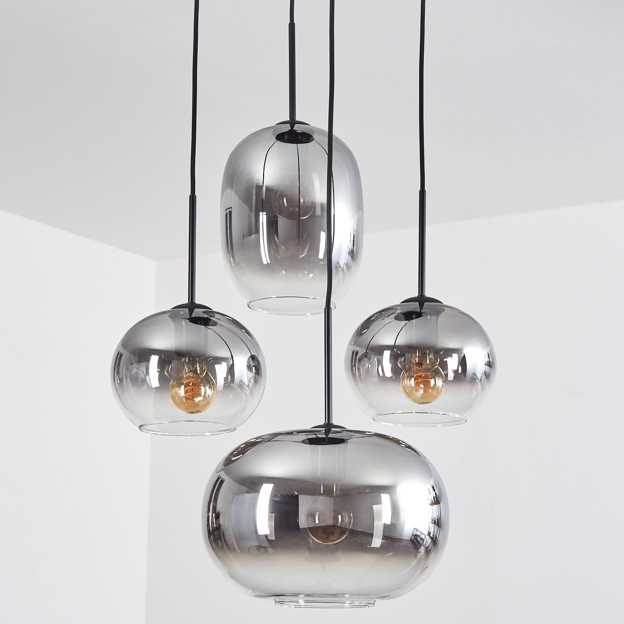 Vier Glaspendelleuchten mit Rauchglas-Finish hängen an schwarzen Kabeln.