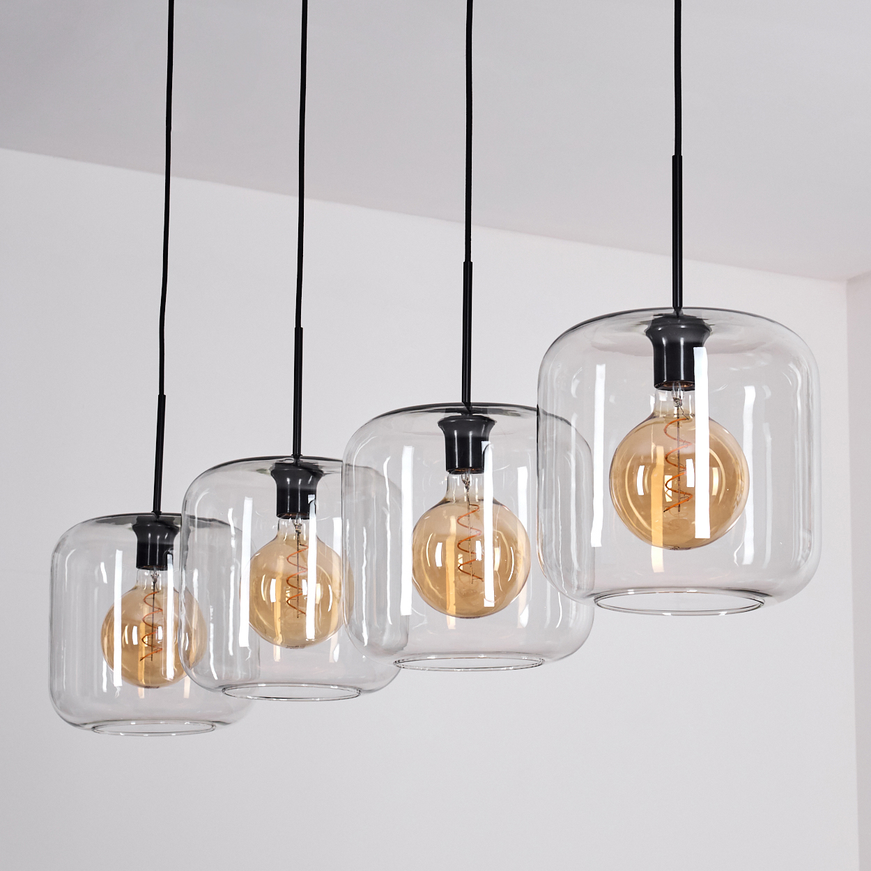 Vier Glaspendelleuchten mit sichtbaren Edison-Glühbirnen hängen von schwarzen Kabeln.