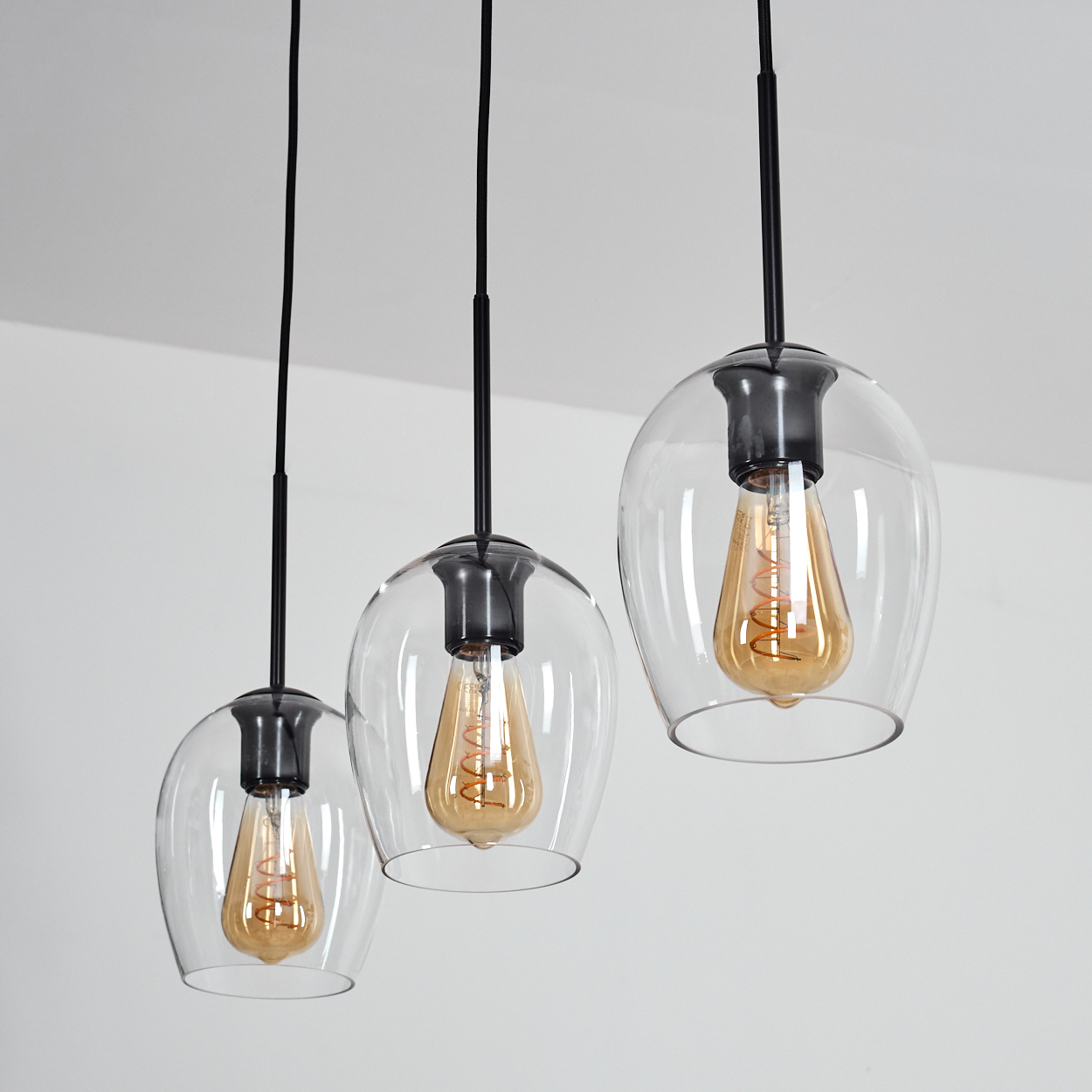 Drei Hängeleuchten mit Glasglocken und sichtbaren Edison-Glühbirnen.