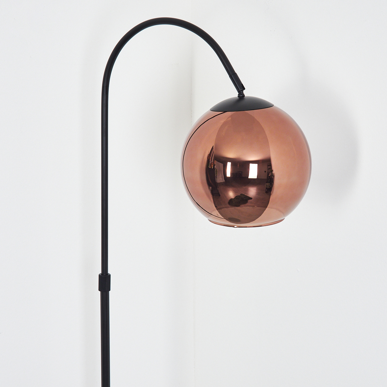 Ein moderner Stehleuchte mit einer kugelförmigen Kupferlampe und schwarzem Gestell.