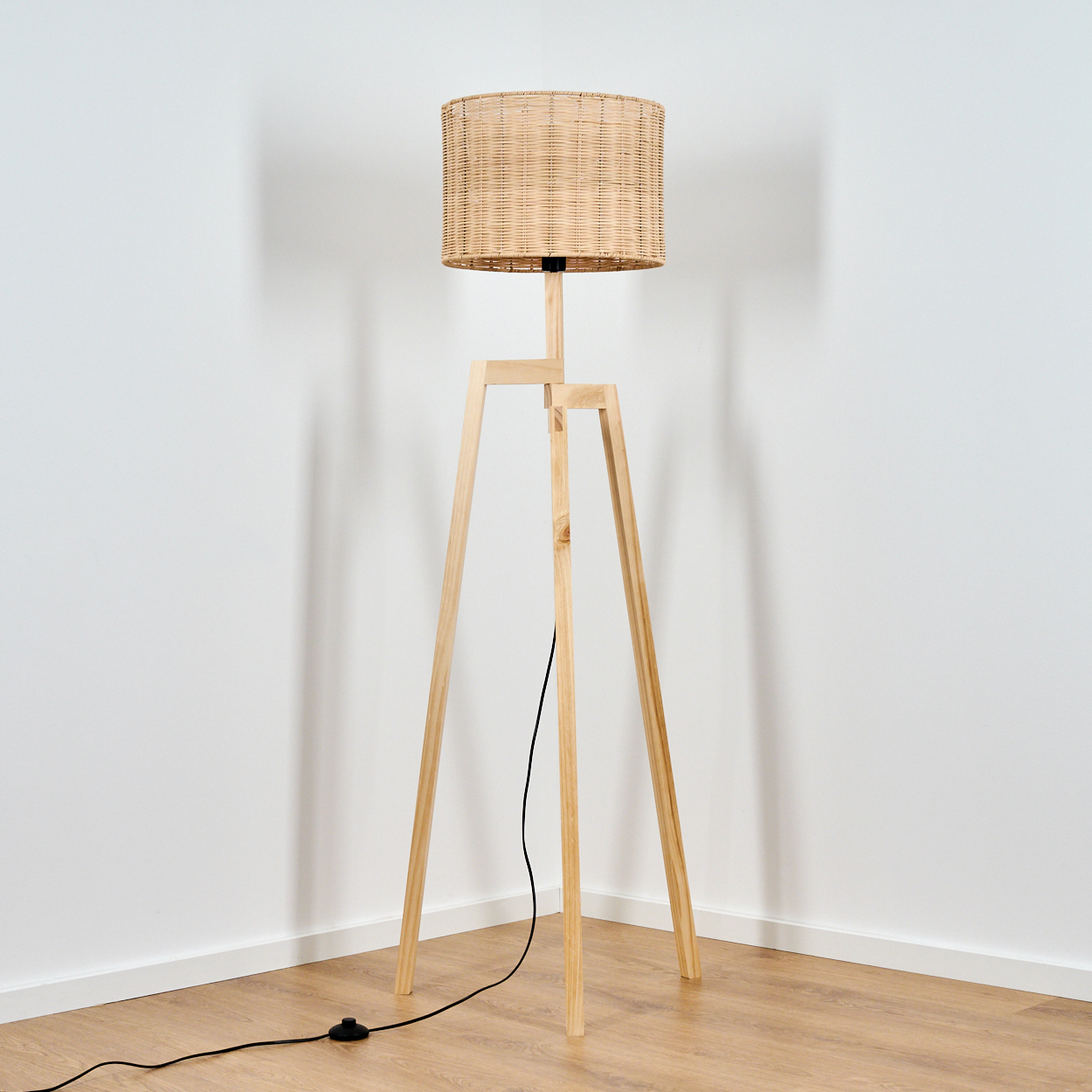 Ein Stehlampe mit Holzstativ und geflochtenem Lampenschirm steht in einer Ecke.
