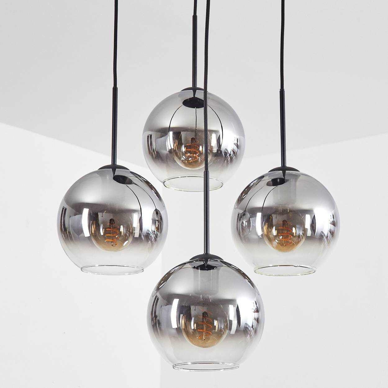 Vier kugelförmige Pendelleuchten mit Rauchglas und sichtbaren Glühbirnen.