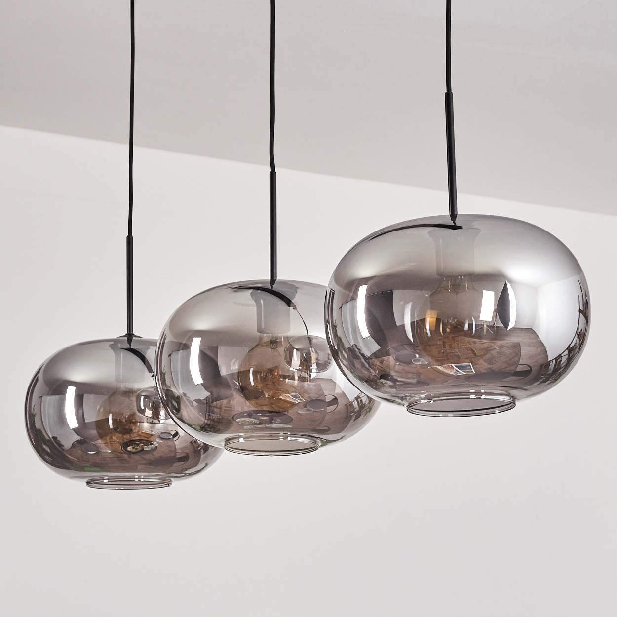 Drei rauchglas Lampenschirme mit Glühbirnen hängen an schwarzen Kabeln.
