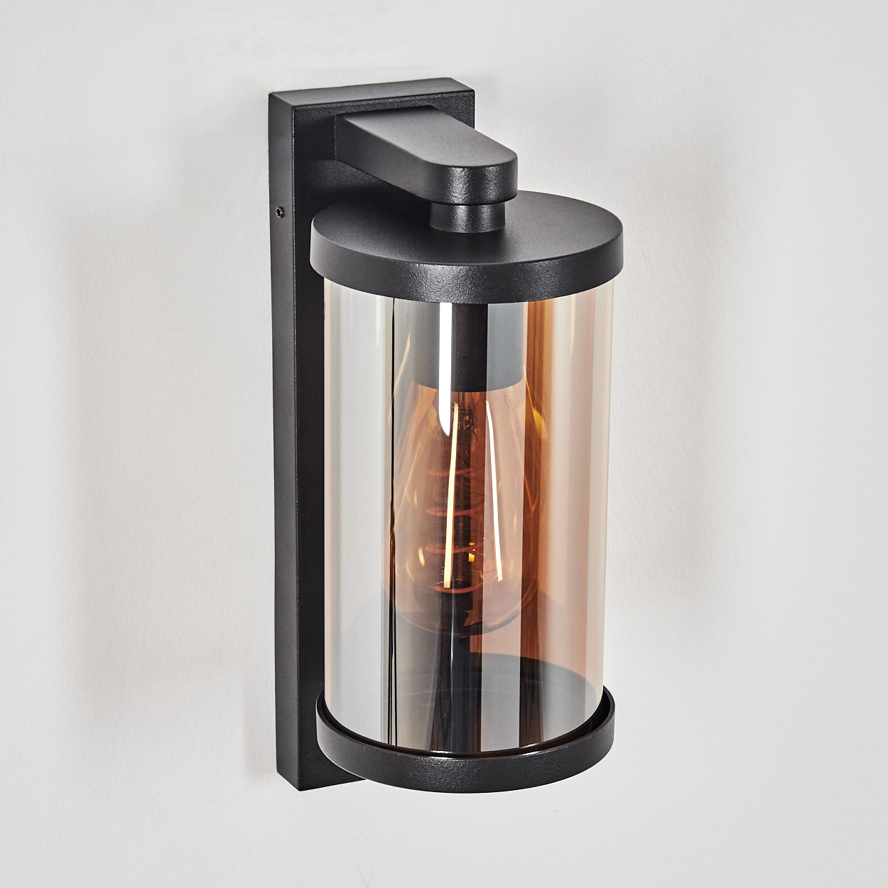 Schwarze Wandleuchte mit zylindrischem Bernstein-Glas und sichtbarer Glühbirne.