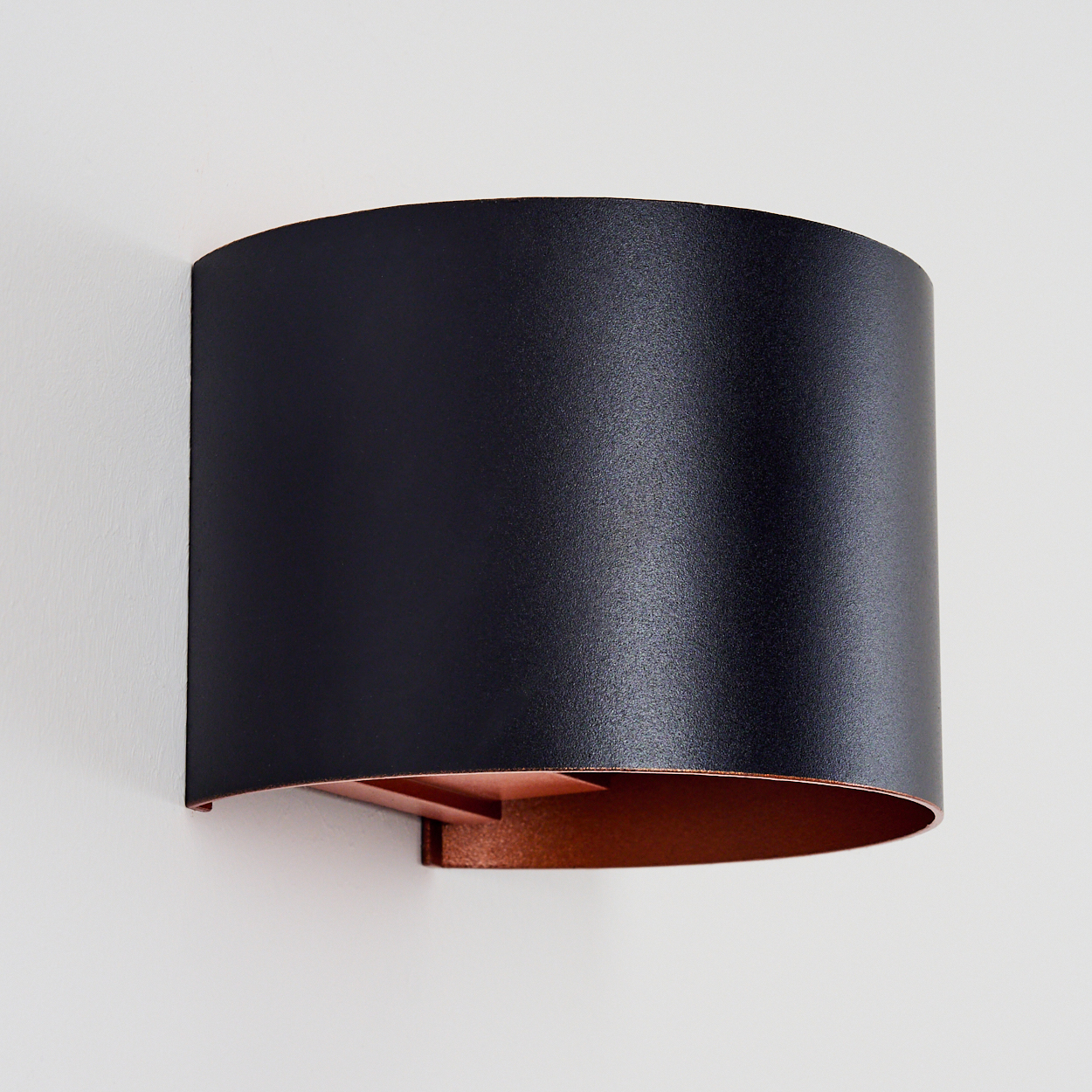 Eine schwarze Wandleuchte mit kupferfarbenem Innenteil an einer weißen Wand.